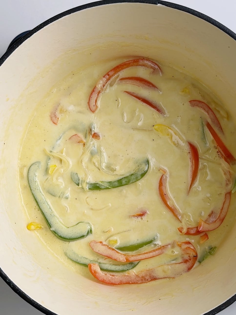 Creamy sauce with bell peppers simmering in a pot for jerk chicken pasta.