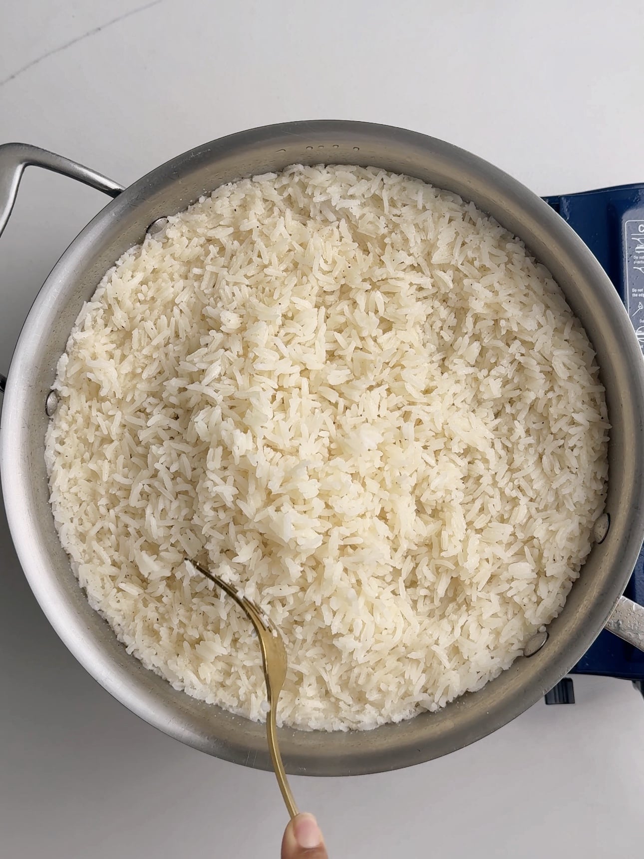 Cooked coconut rice in a skillet being fluffed with a fork.