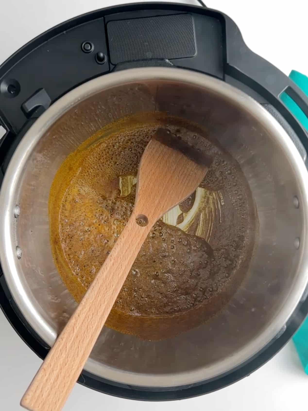 Oil and curry powder toasting in the bottom of an Instant Pot with a wooden spoon.