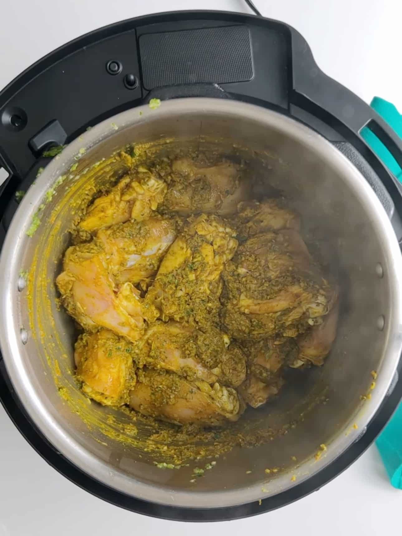 Seasoned chicken cooking in an Instant Pot with green herb seasoning and curry spices.