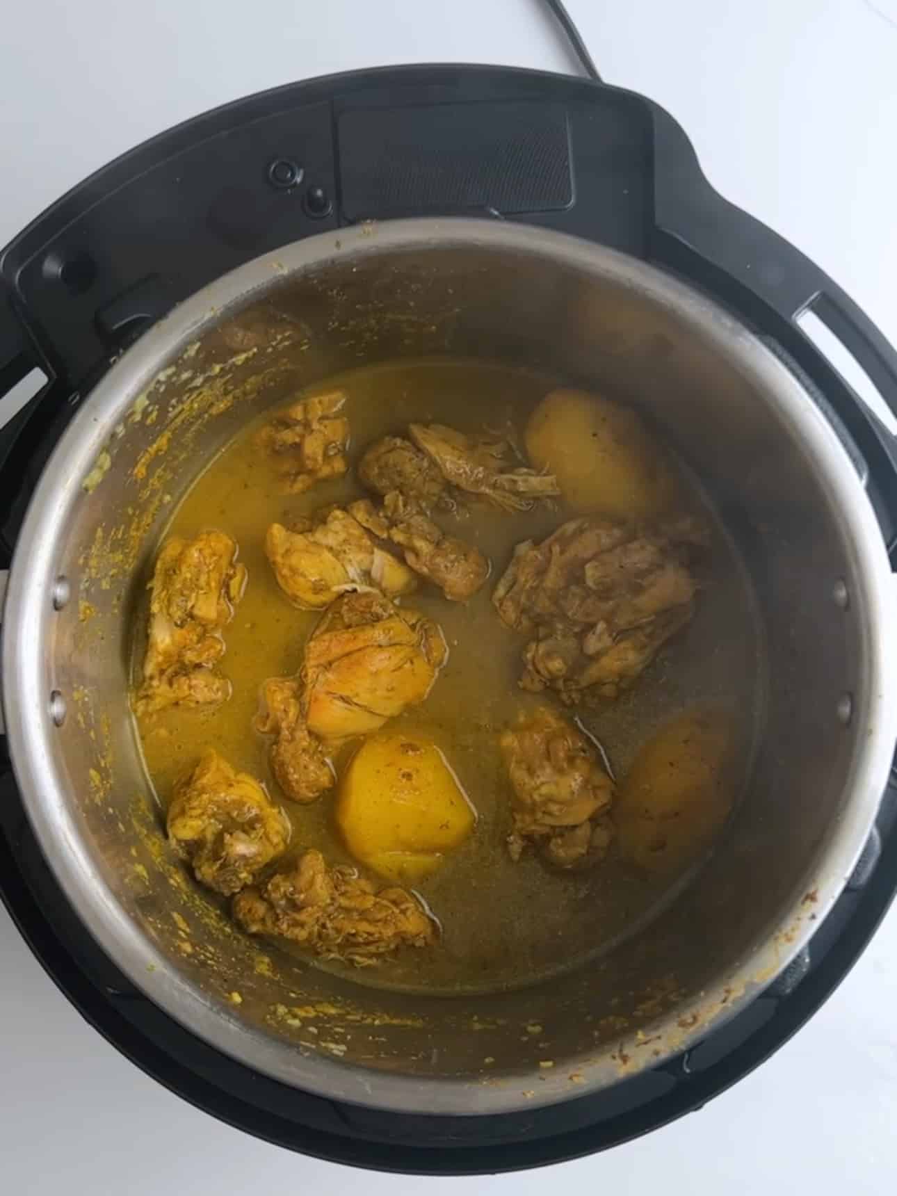 Chicken and potatoes simmering in curry broth inside an Instant Pot.