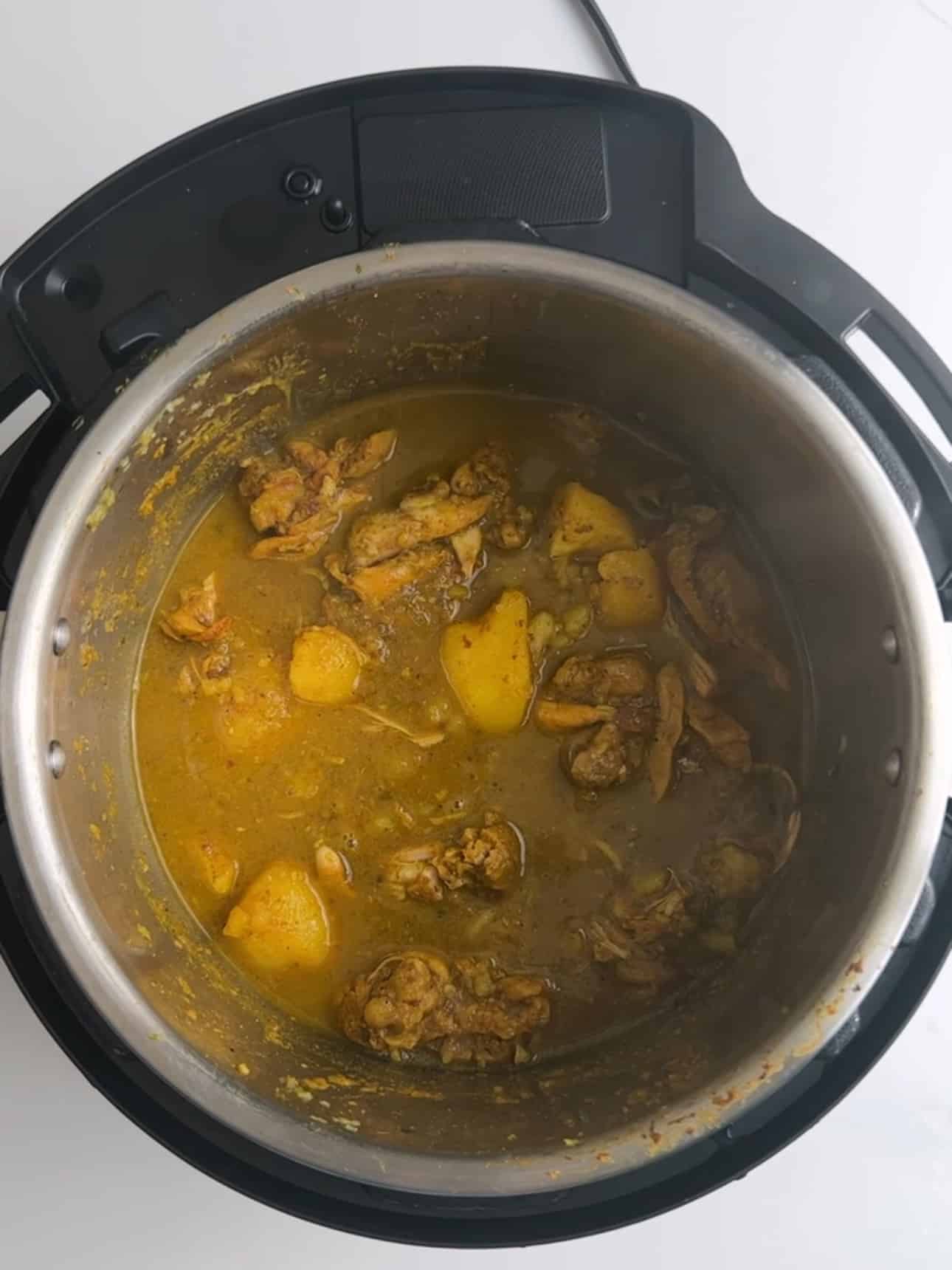 Chicken and potatoes simmering in curry broth inside an Instant Pot.