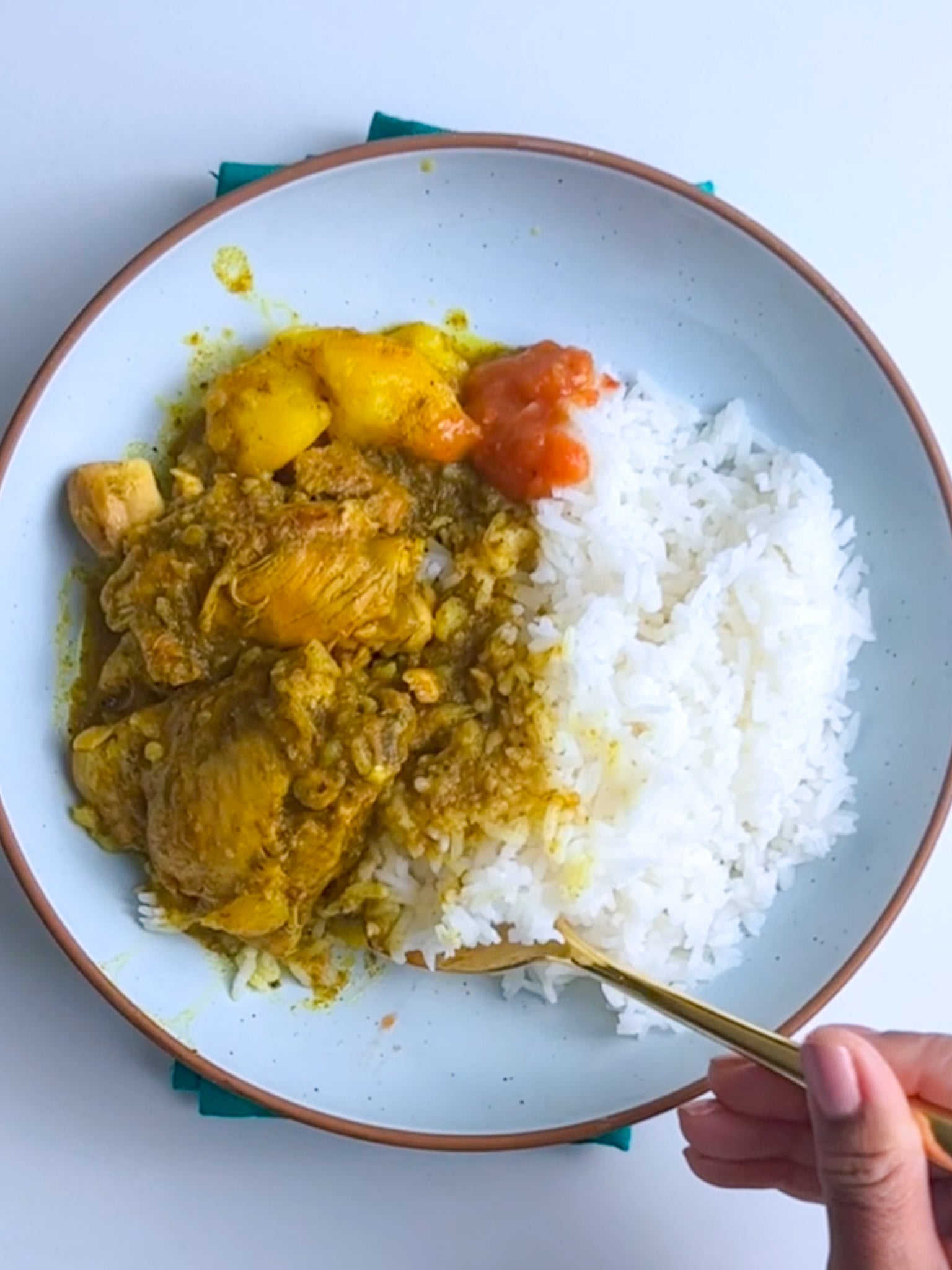 late of Guyanese chicken curry with potatoes served over white rice, topped with a small spoonful of pepper sauce.