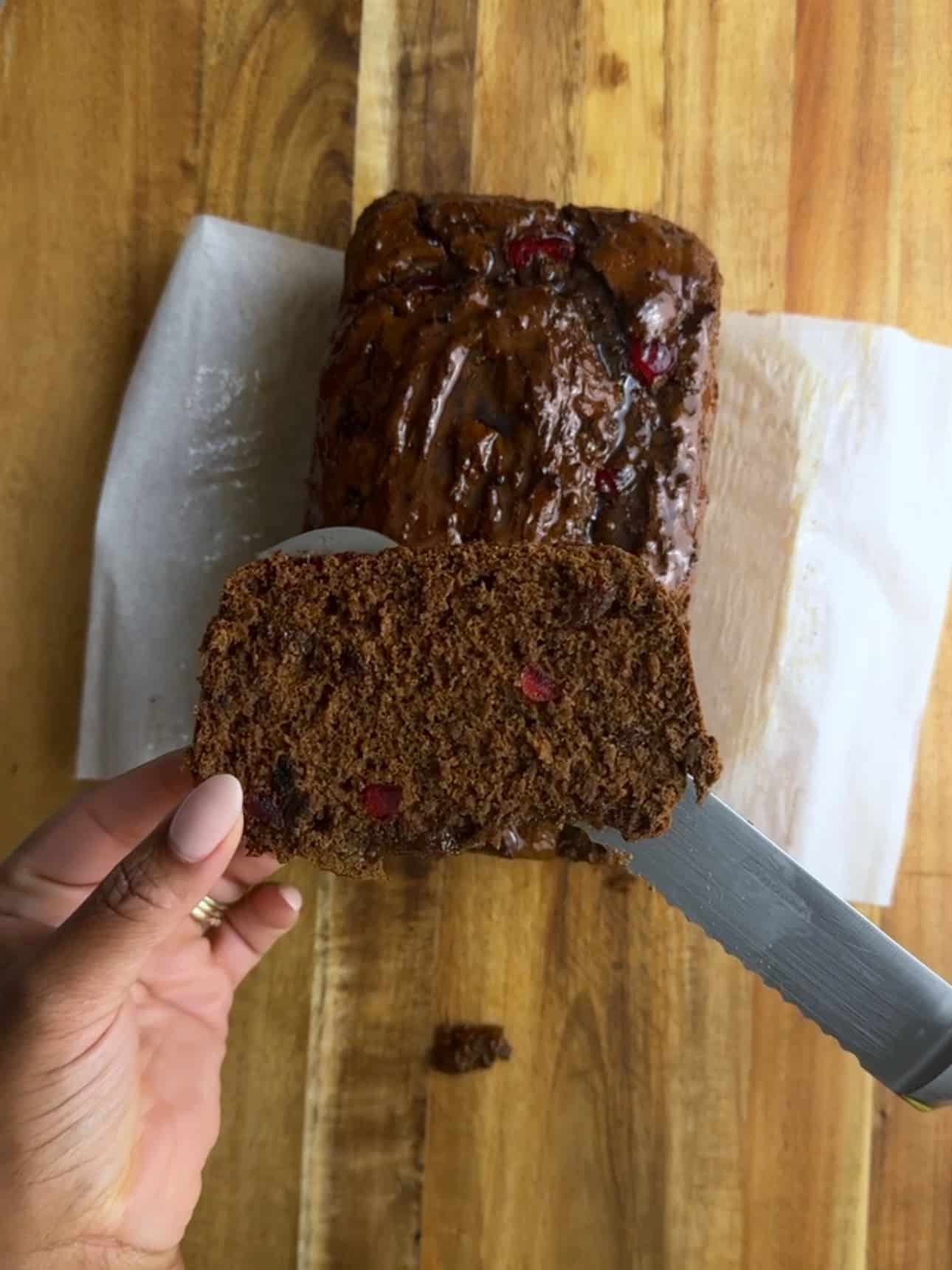 A slice of Jamaican Easter bun being cut from a loaf on parchment paper.