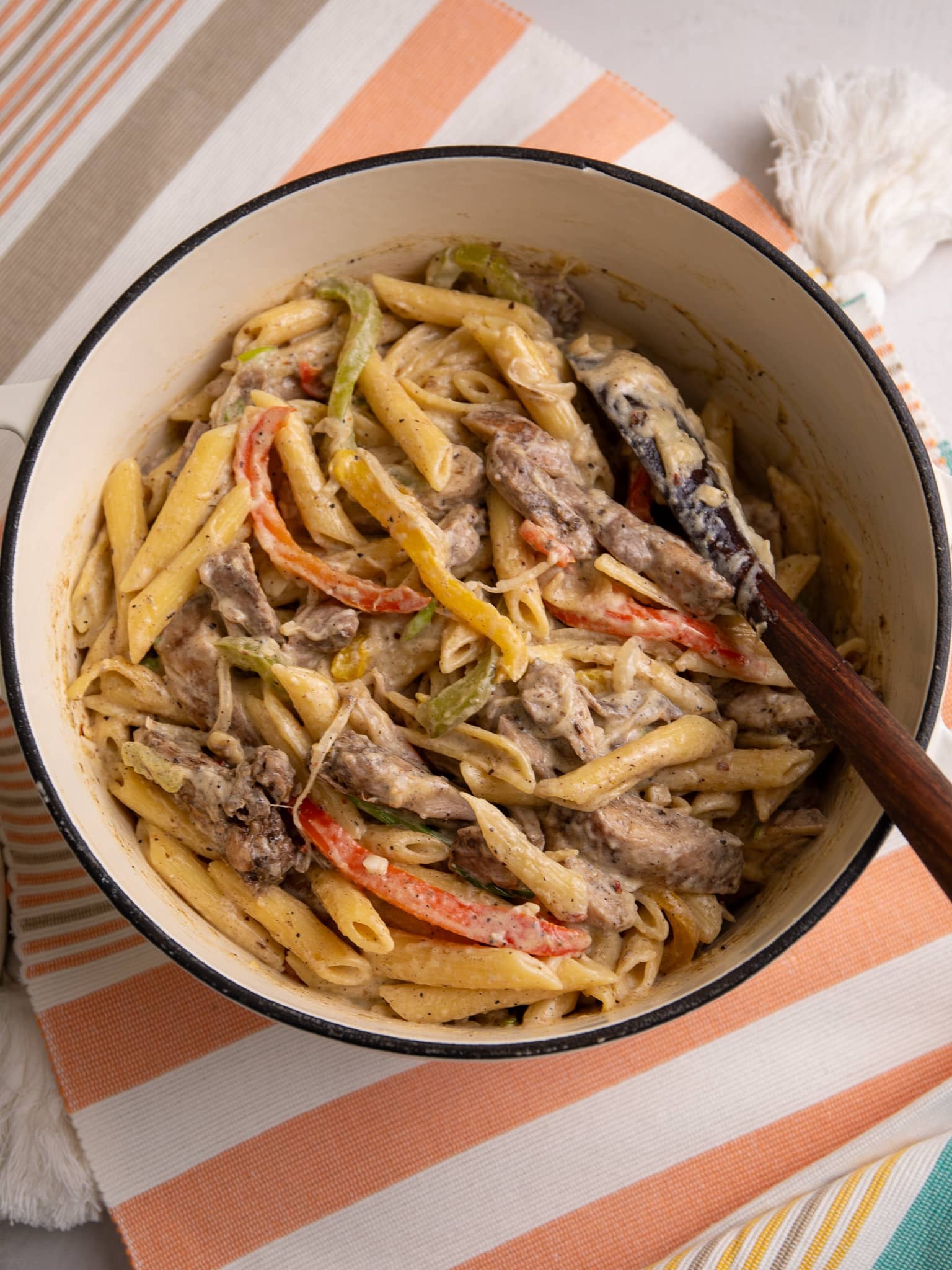Jerk chicken rasta pasta being tossed together in a large pot with peppers and creamy sauce.