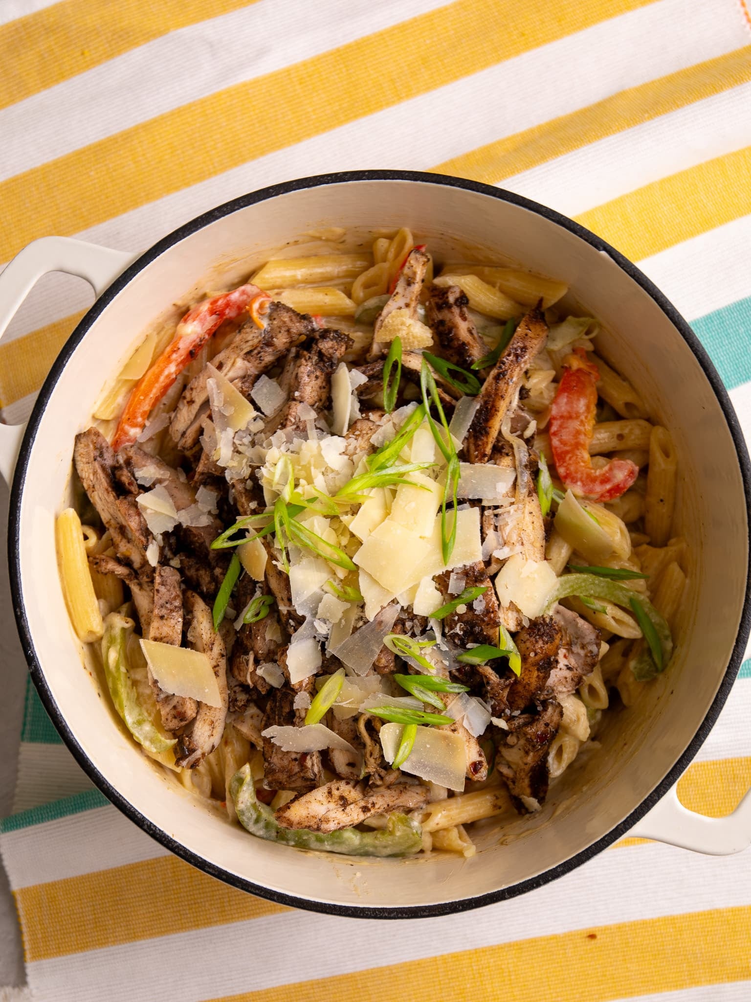 Jerk chicken pasta topped with shaved parmesan and scallions in a cream sauce with bell peppers.