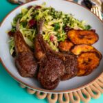 Plate of pan seared lamb chops served with salad and fried plantains.
