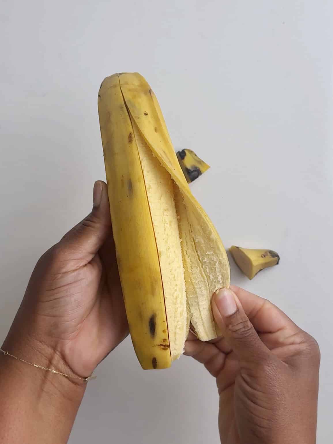 Hand holding peeled yellow plantains.
