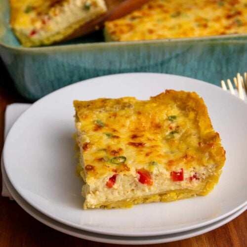 A slice of plantain quiche served on a white plate with the full baked quiche in the background.
