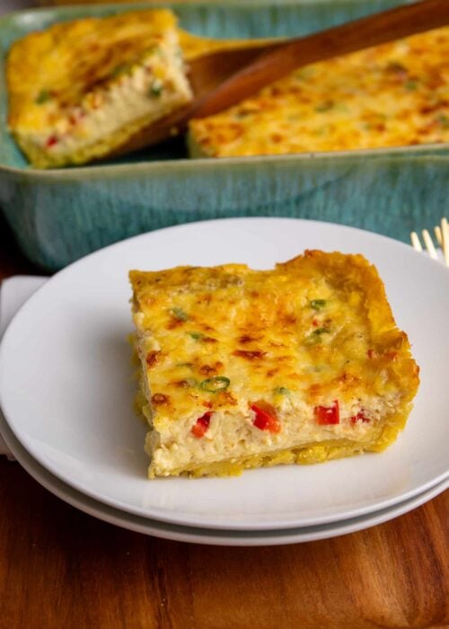 A slice of plantain quiche served on a white plate with the full baked quiche in the background.