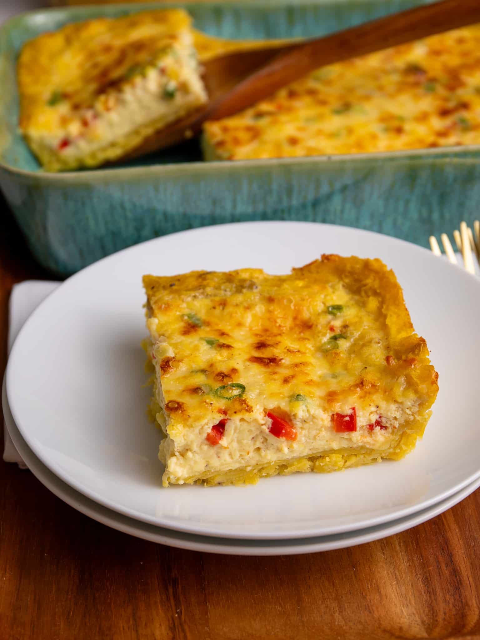 A slice of plantain quiche served on a white plate with the full baked quiche in the background.