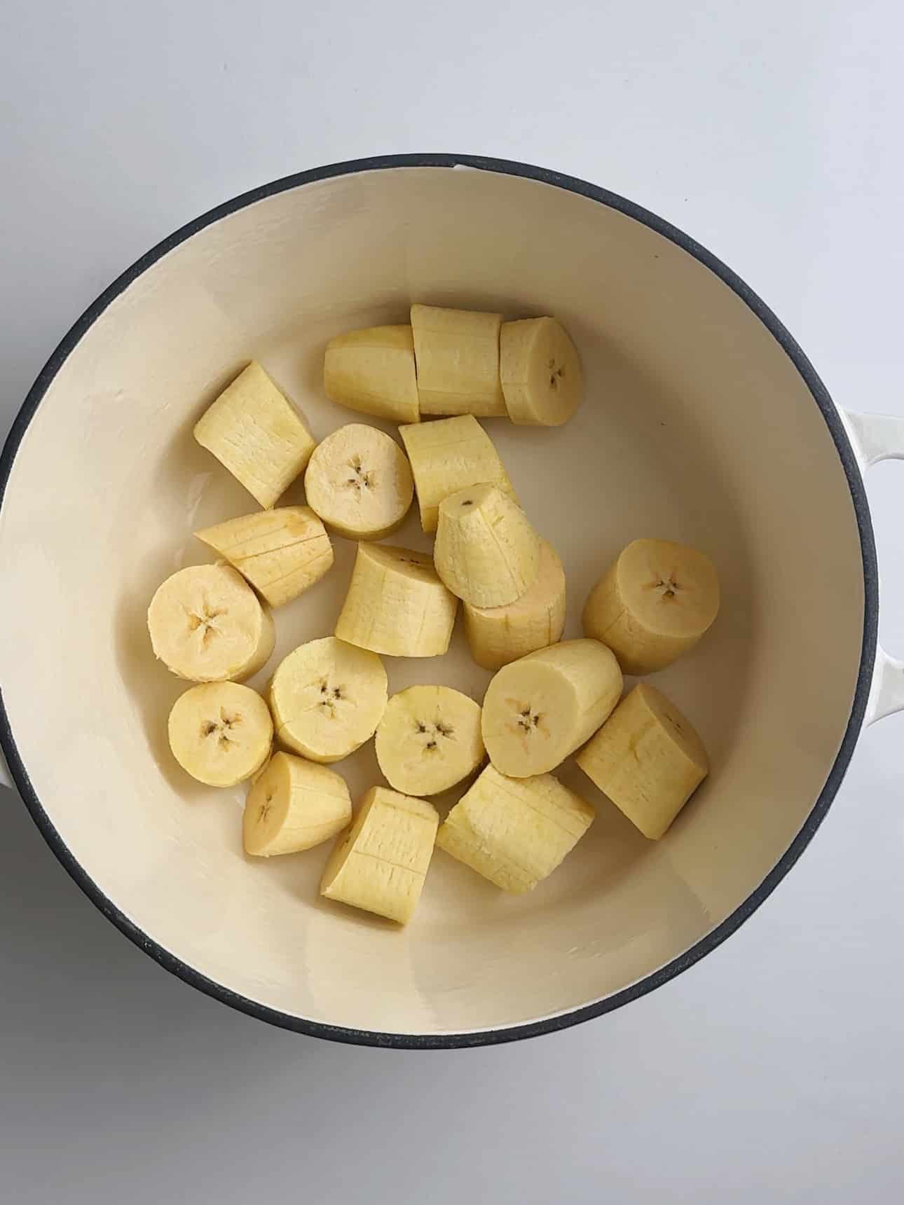 Raw plantain pieces cut into chunks in a pot before cooking.