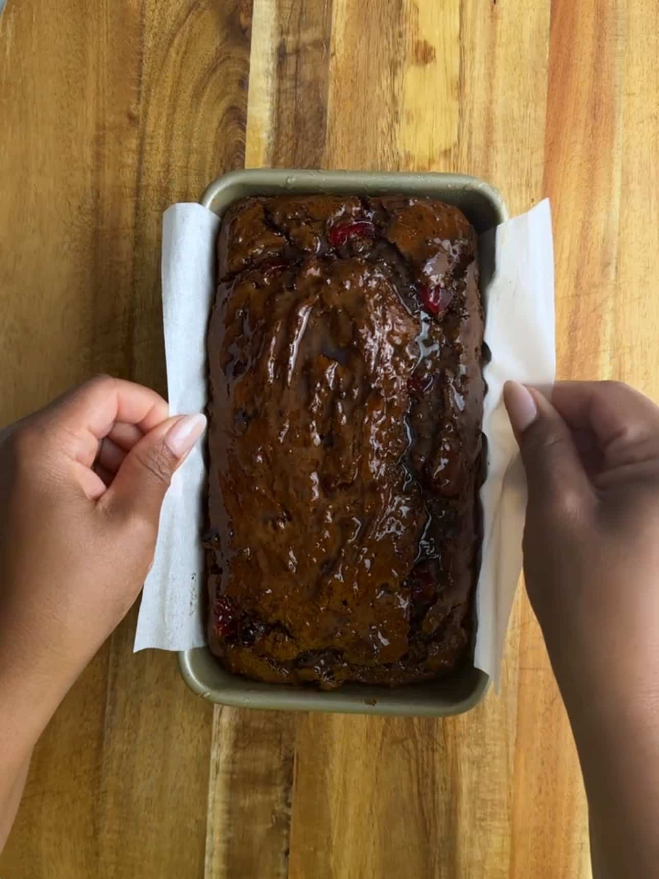 Hands adjusting parchment paper around a freshly baked Jamaican Easter bun in a loaf pan.