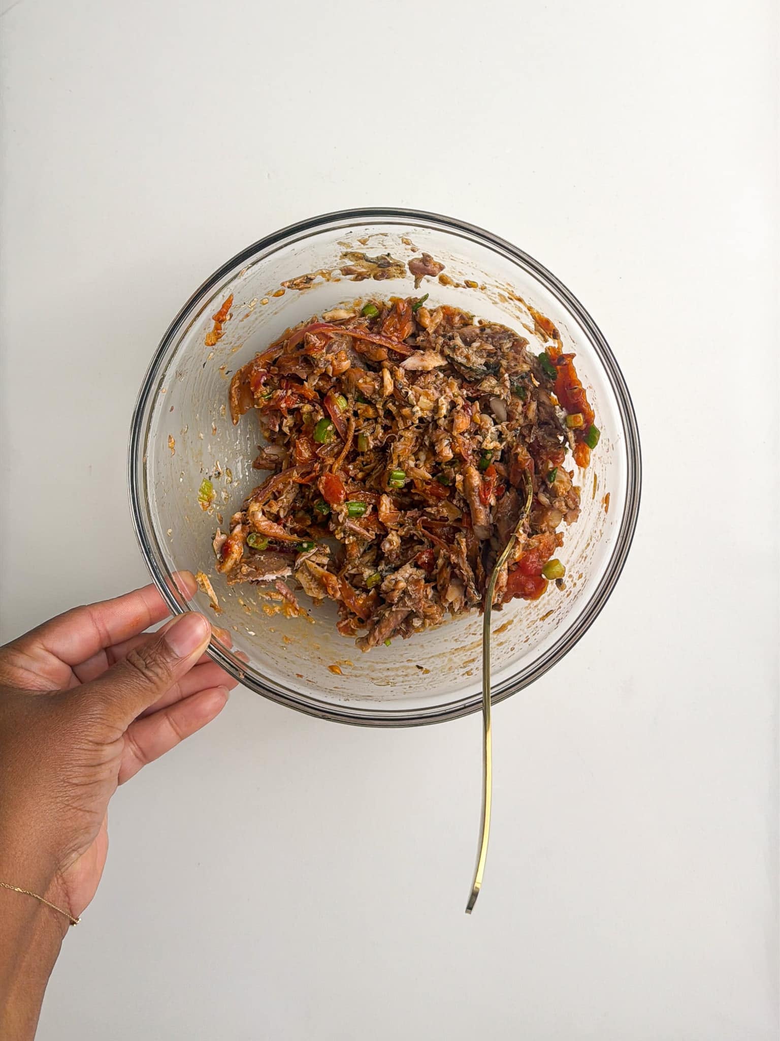 A bowl of mashed sardines mixed with aromatics being stirred with a spoon.