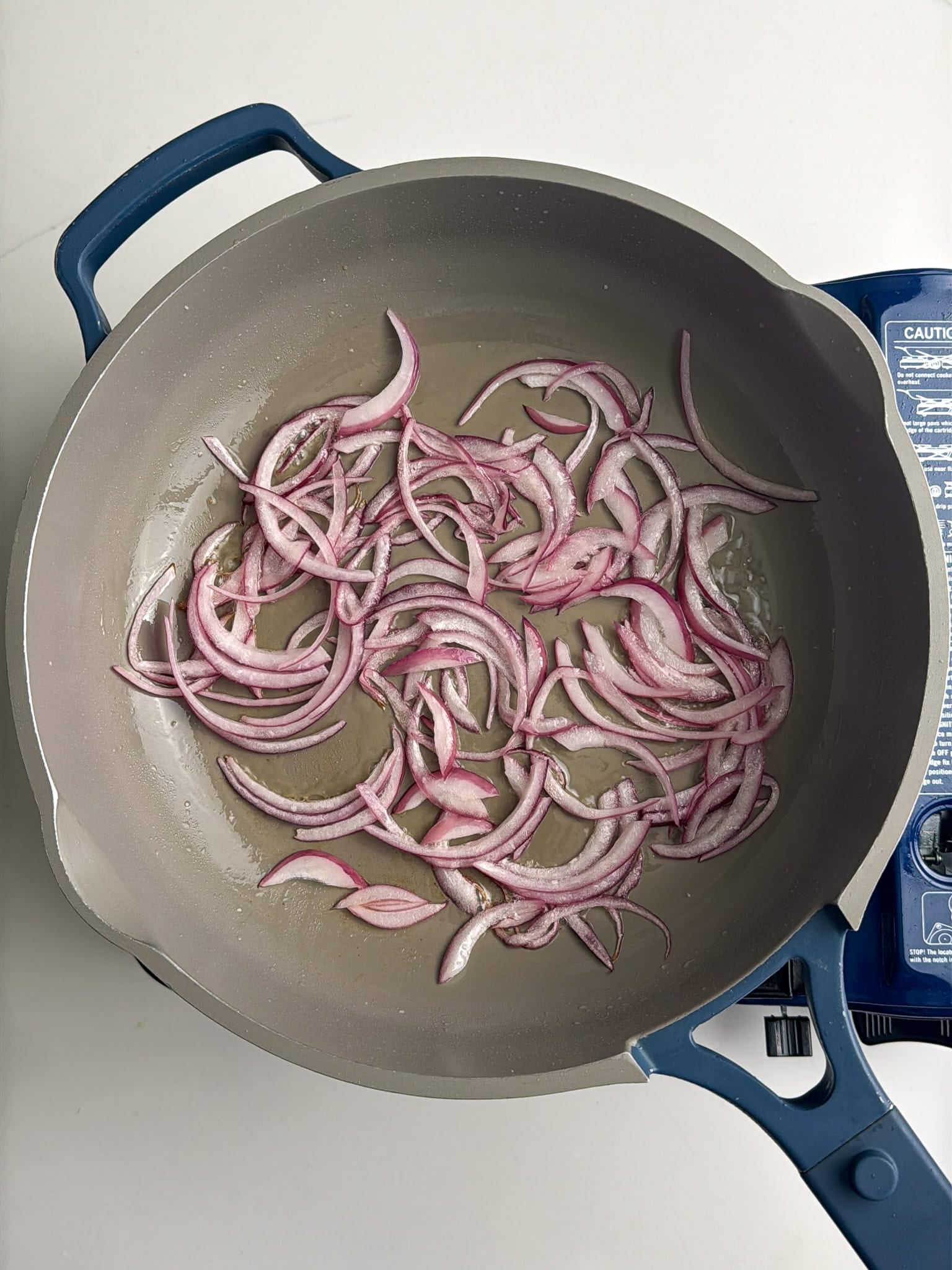 A pan with thinly sliced red onions cooking in oil on the stovetop.