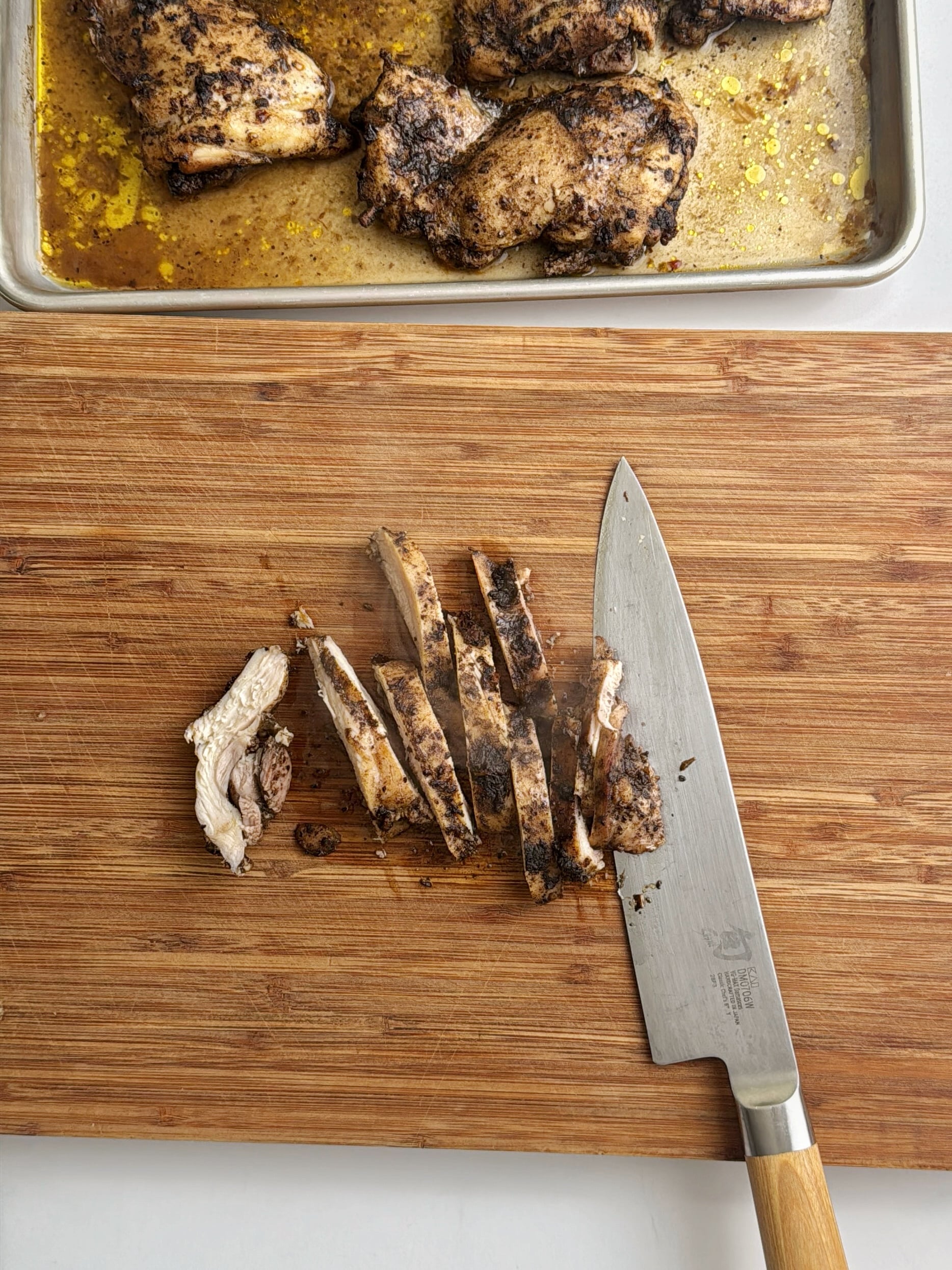 Cooked jerk chicken being sliced into strips on a wooden cutting board.