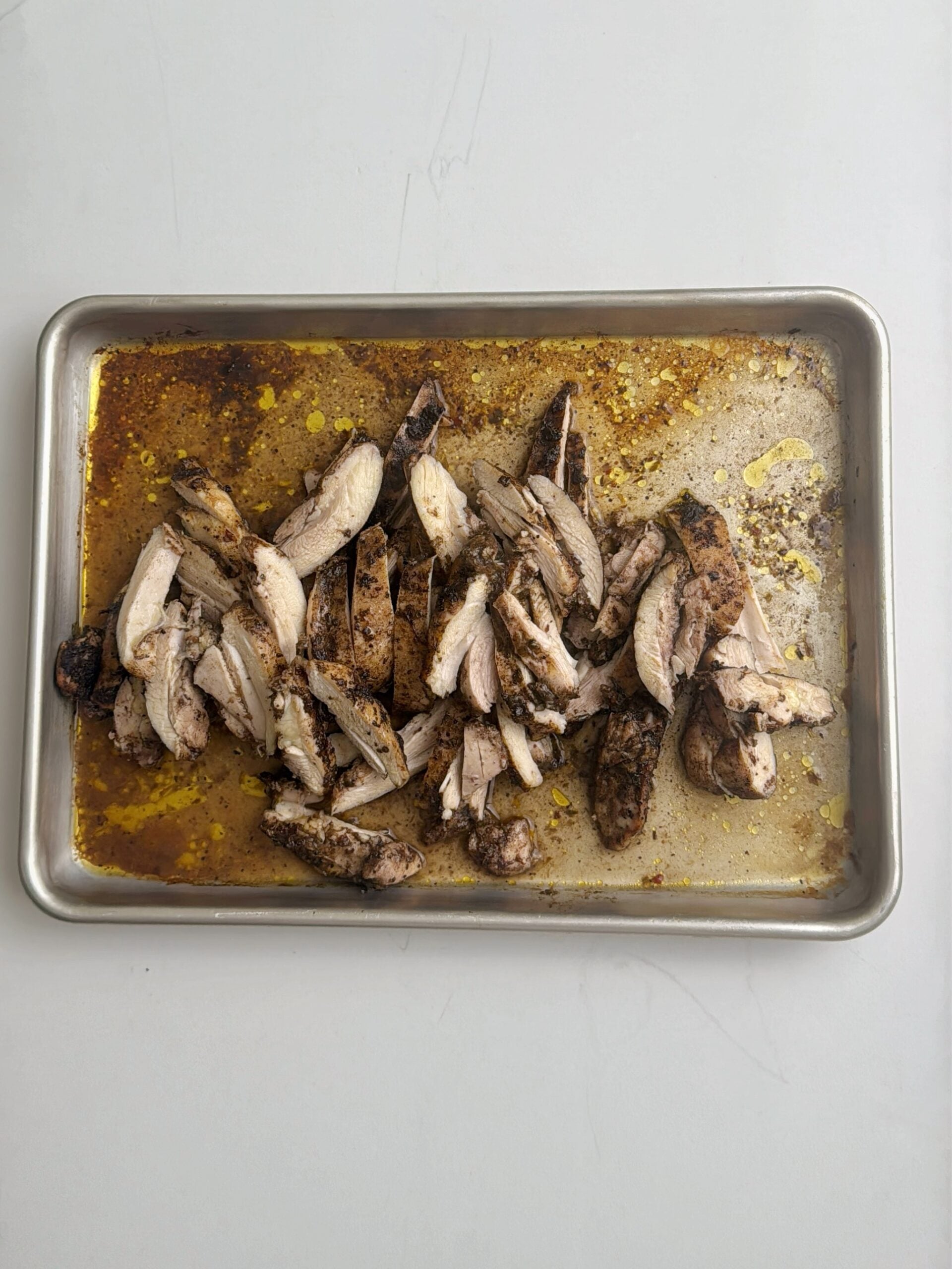 Sliced jerk chicken returning to the baking sheet with flavorful pan juices.