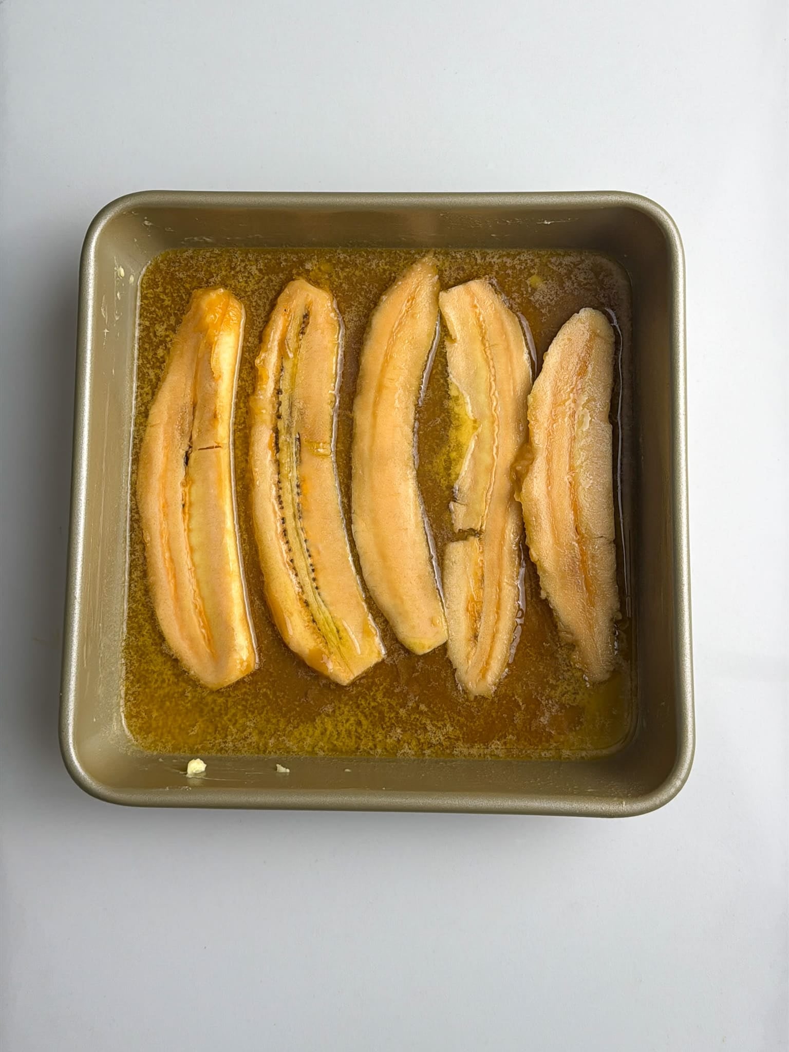 Sliced plantains arranged in a baking pan with melted butter and sugar.