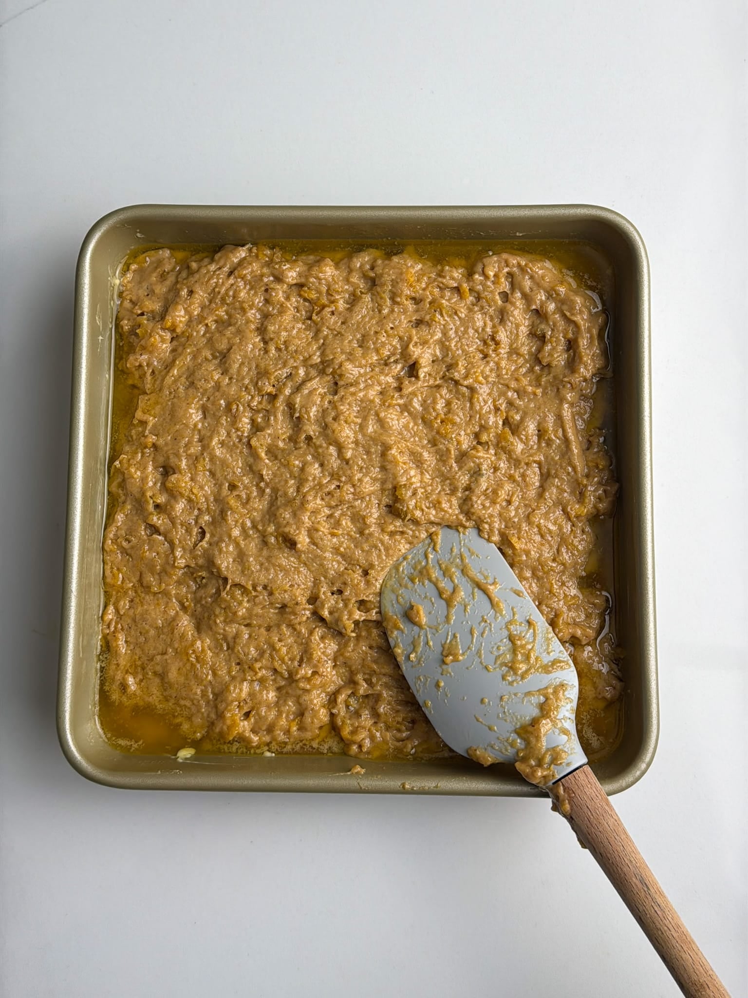 Plantain batter being spread over sliced plantains in a baking pan.