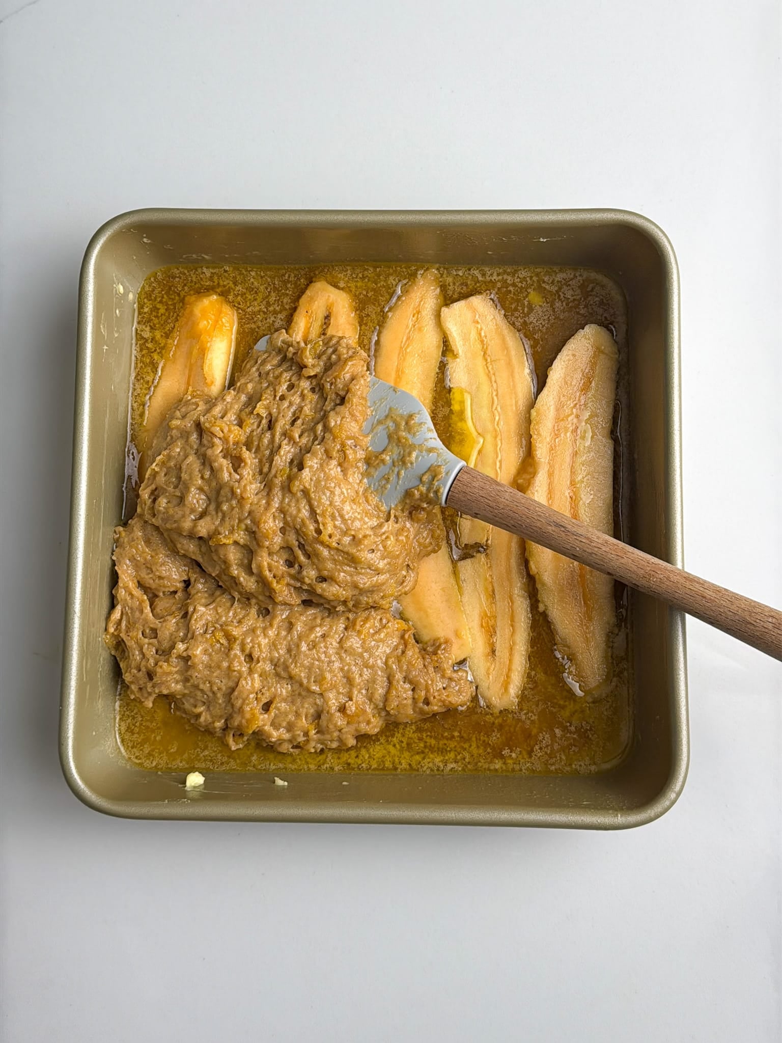 Plantain batter being spread over sliced plantains in a baking pan.