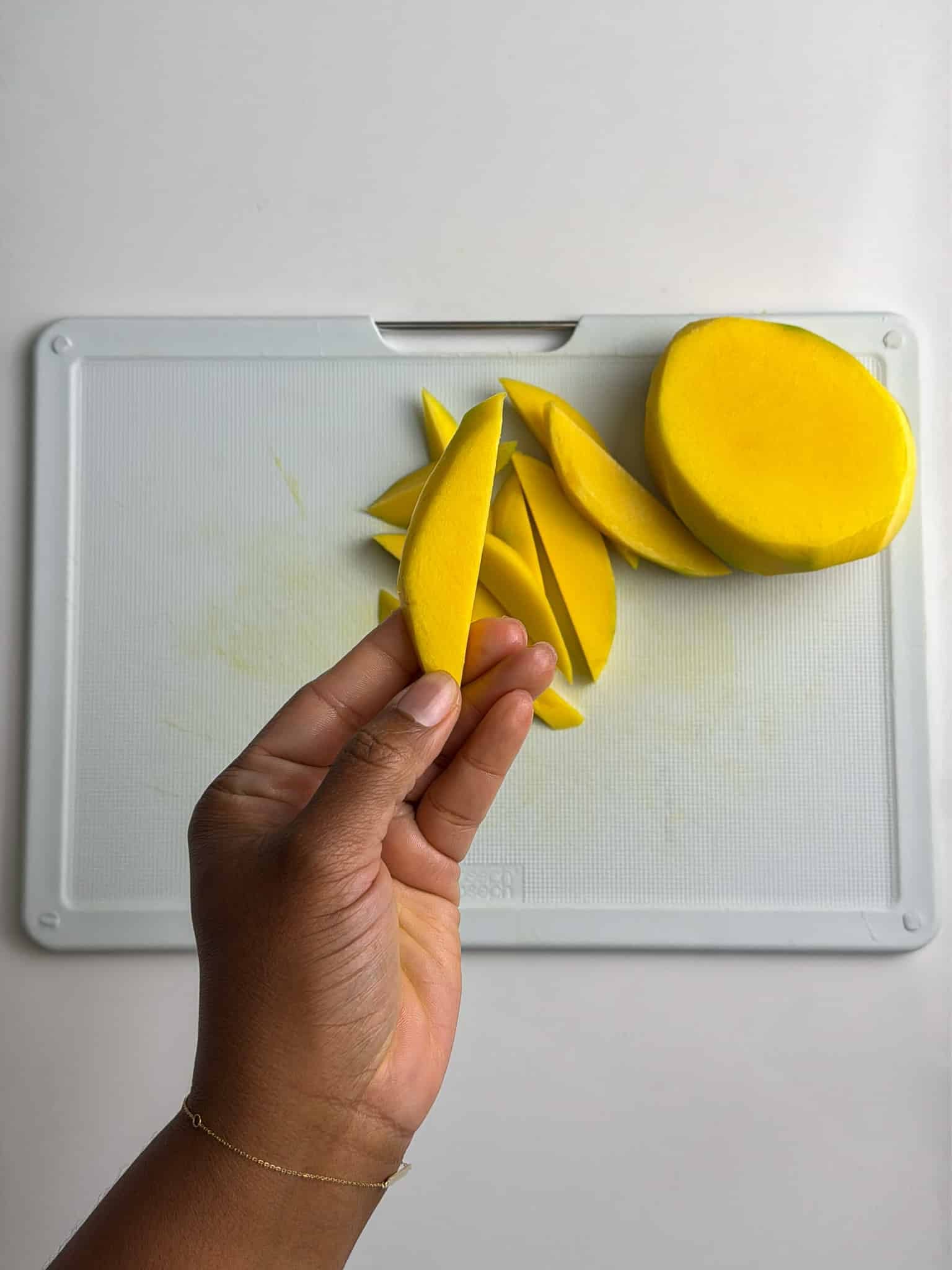 Hand holding freshly sliced green mango strips on a cutting board.