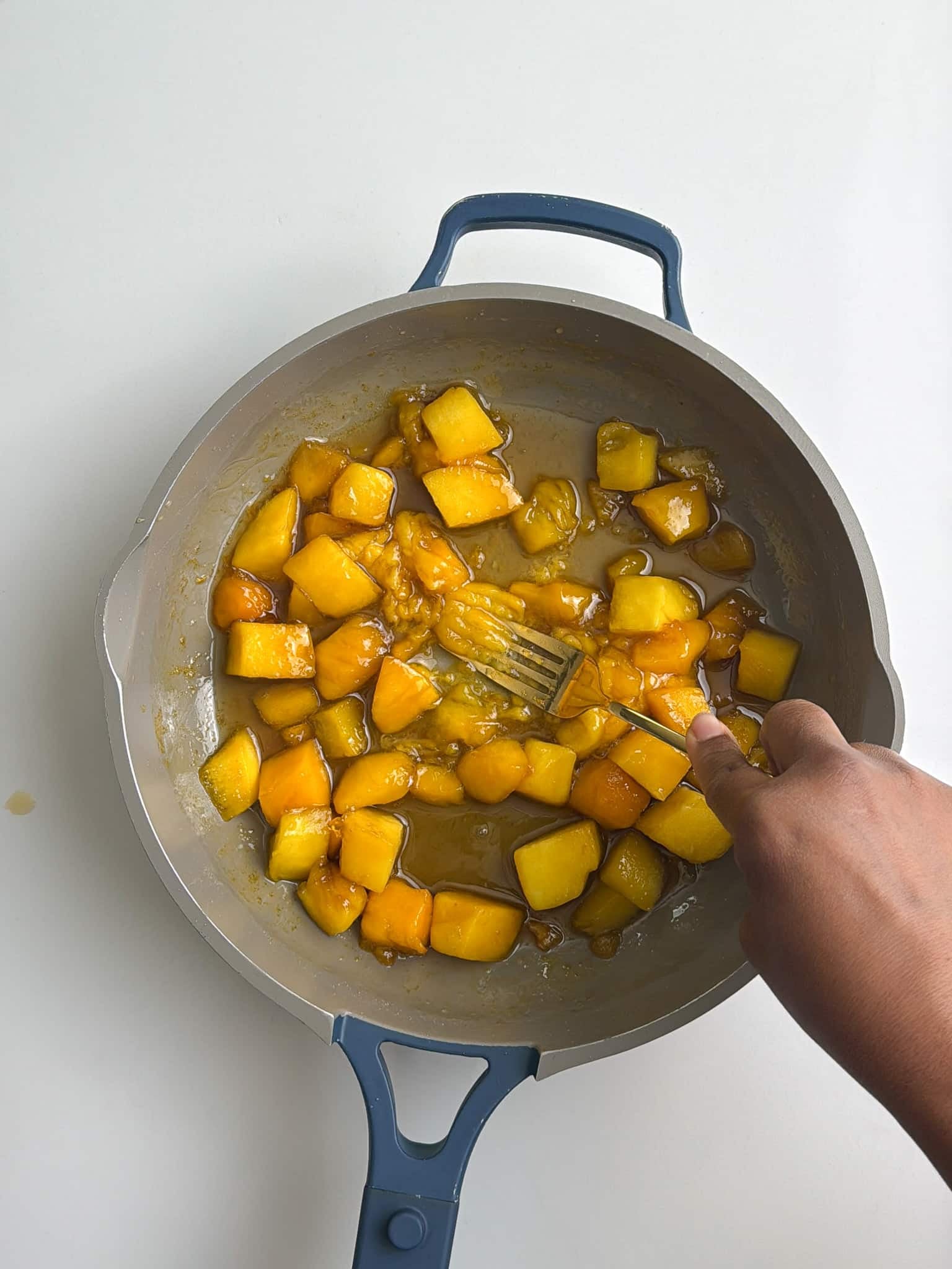 Fresh diced mango being stirred in a saucepan before fully breaking down.