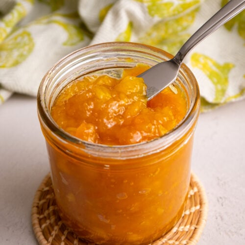 Close-up of thick, glossy mango jam in a jar showing its texture.