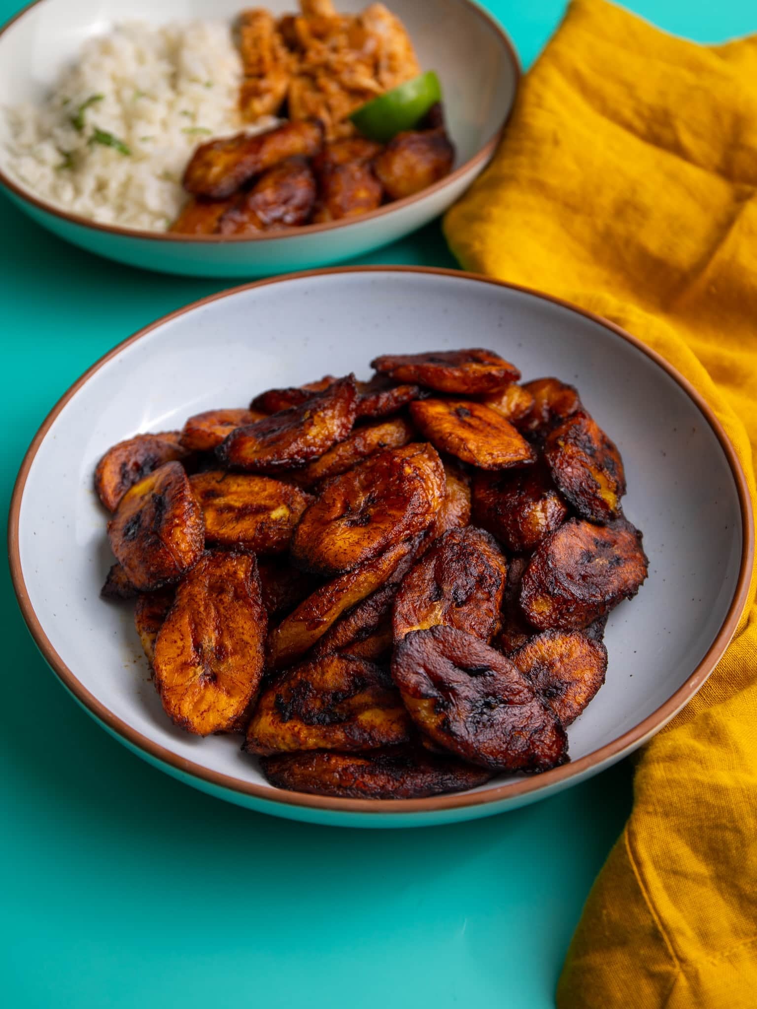 Bowl of fried plantains served on a teal background.