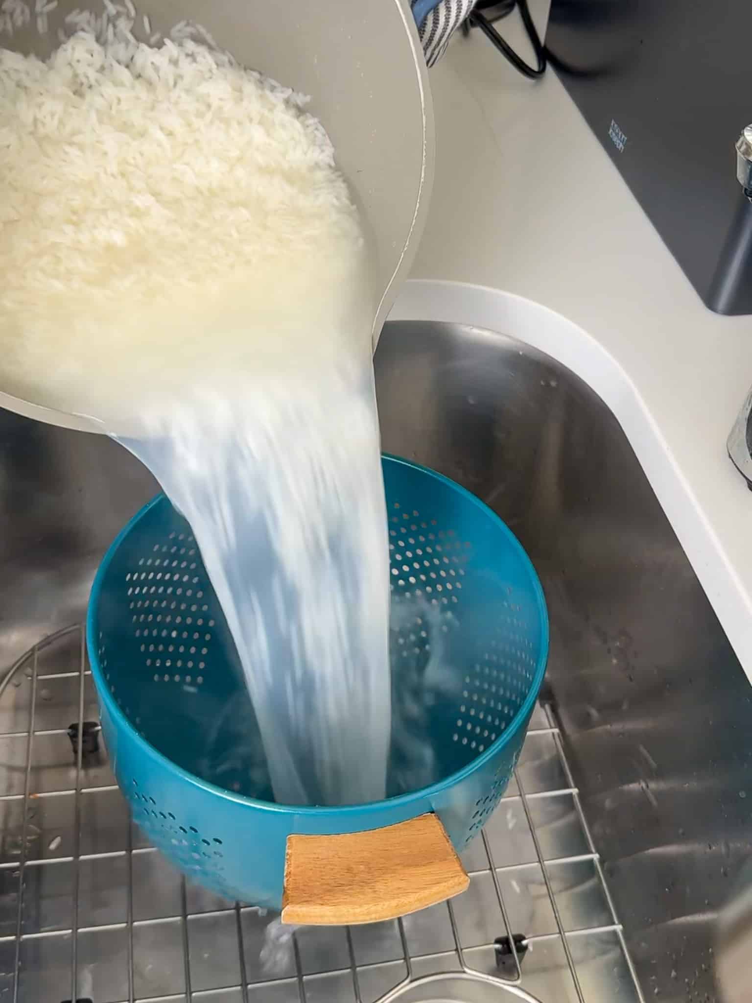 Cooked white rice being drained through a colander after boiling in water