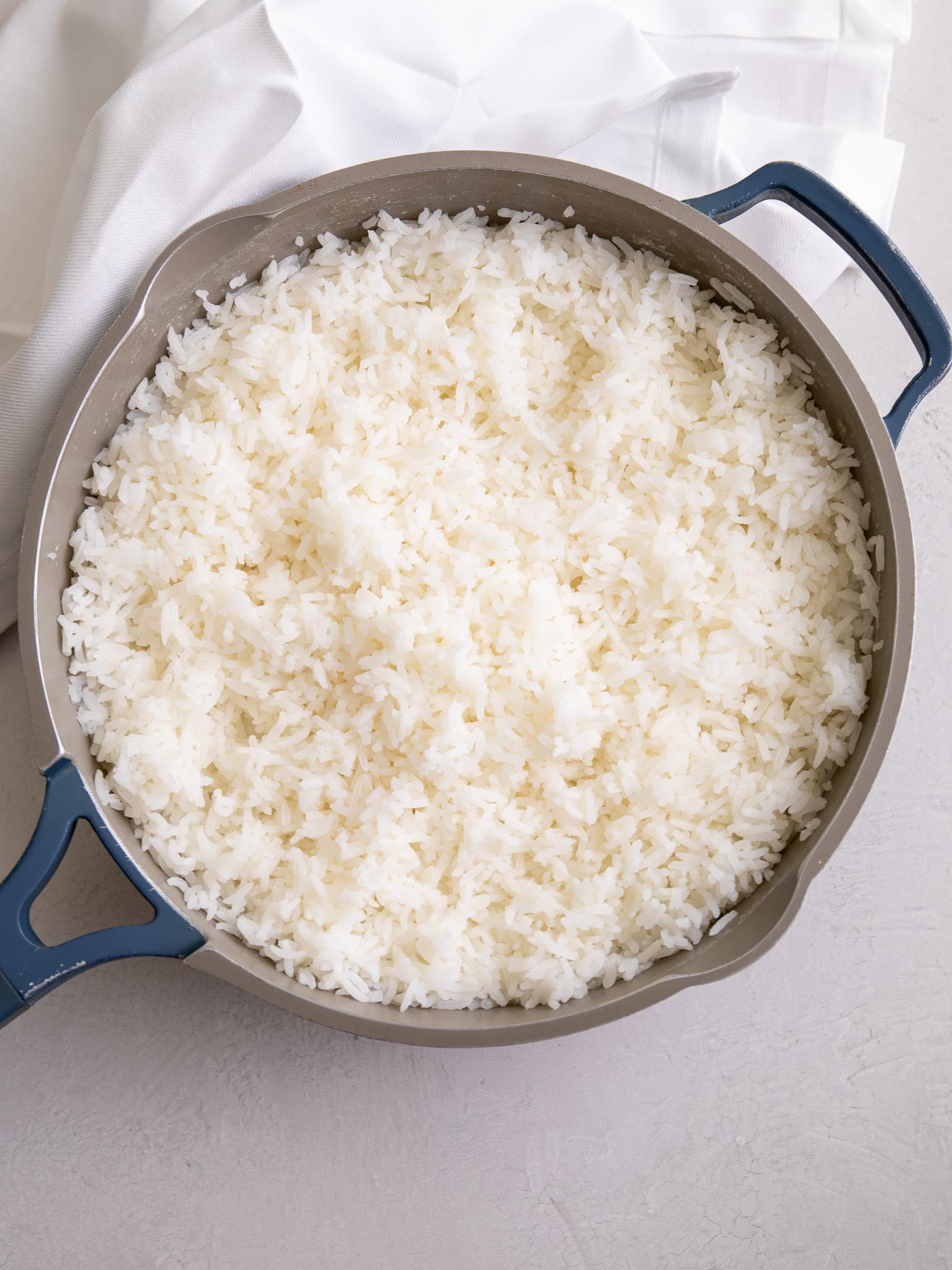 A pot of freshly cooked white rice with fluffy, separate grains, shown in a wide pan on a light surface.