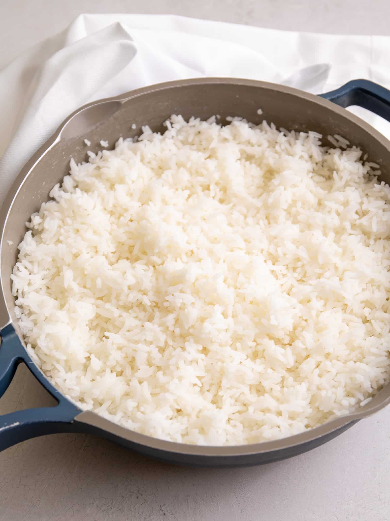 A pot of freshly cooked white rice with fluffy, separate grains, shown in a wide pan on a light surface.