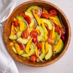 A finished mango avocado salad in a wooden bowl with sliced mango, avocado, cherry tomatoes, and red onion.