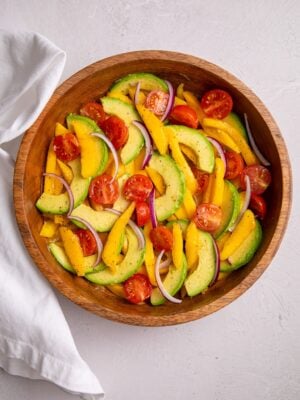 A finished mango avocado salad in a wooden bowl with sliced mango, avocado, cherry tomatoes, and red onion.