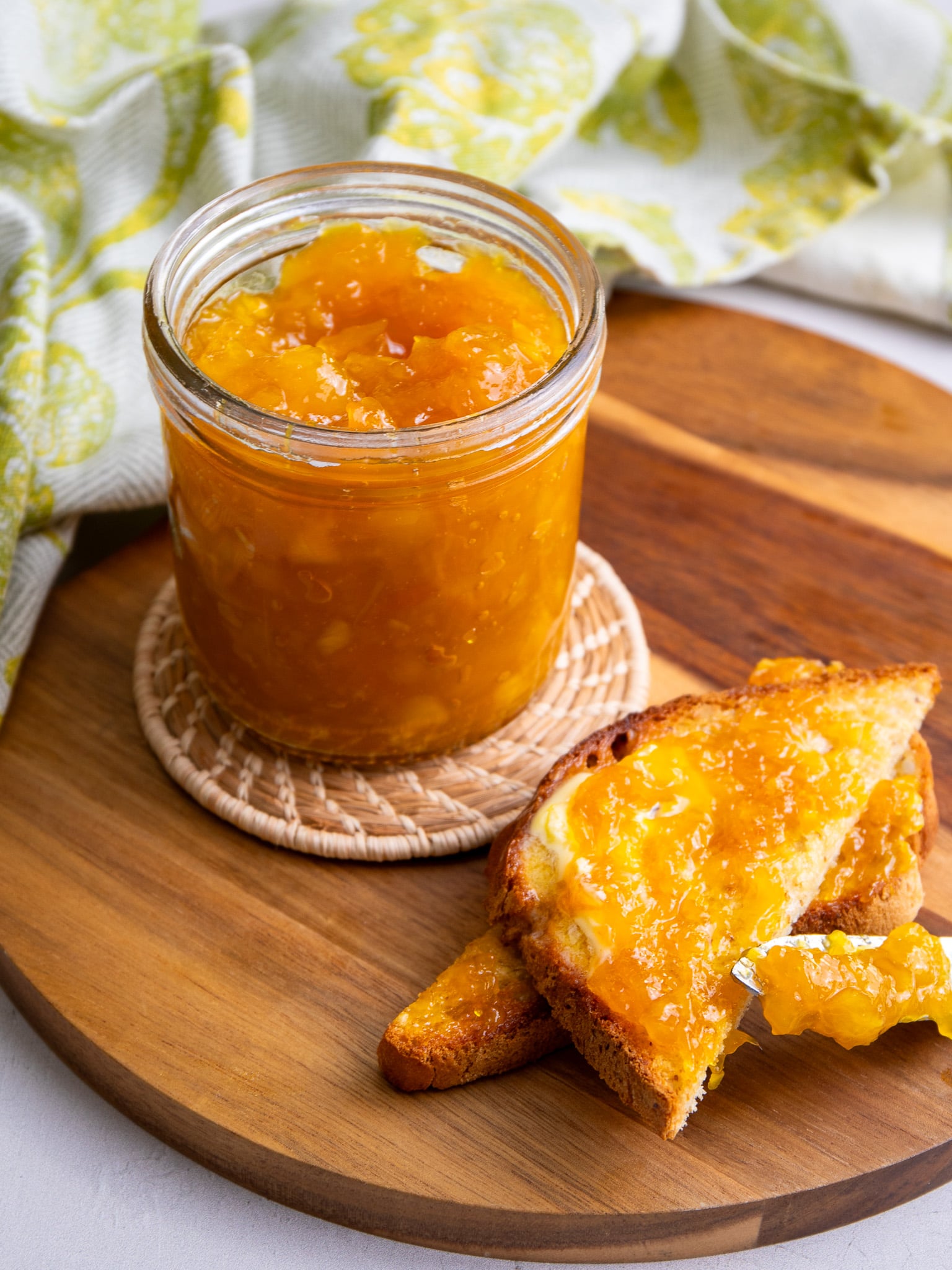 A jar of mango jam served with buttered toast on a wooden board.