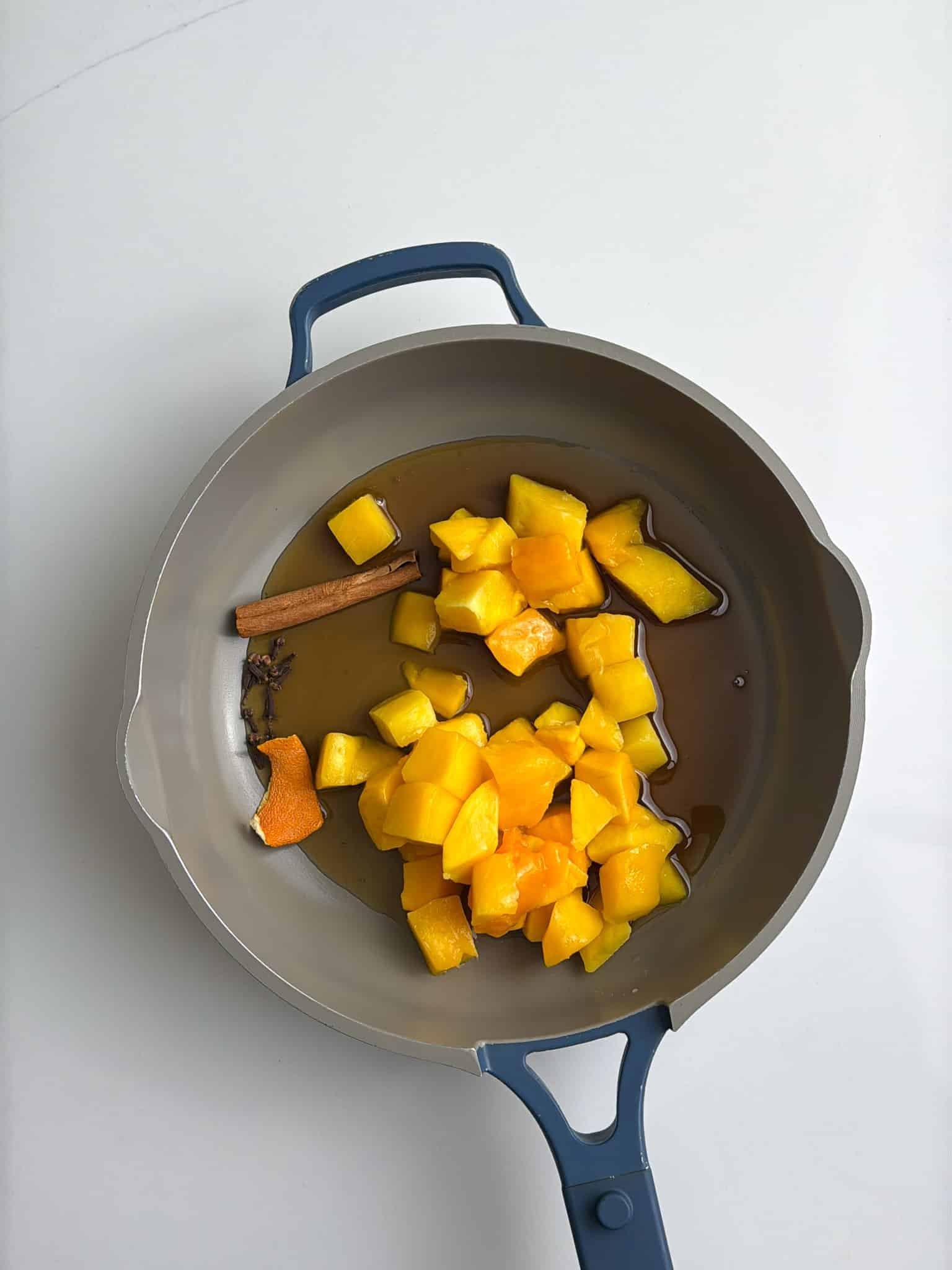 Diced mango and whole spices (cinnamon stick and cloves) added to a saucepan before cooking.