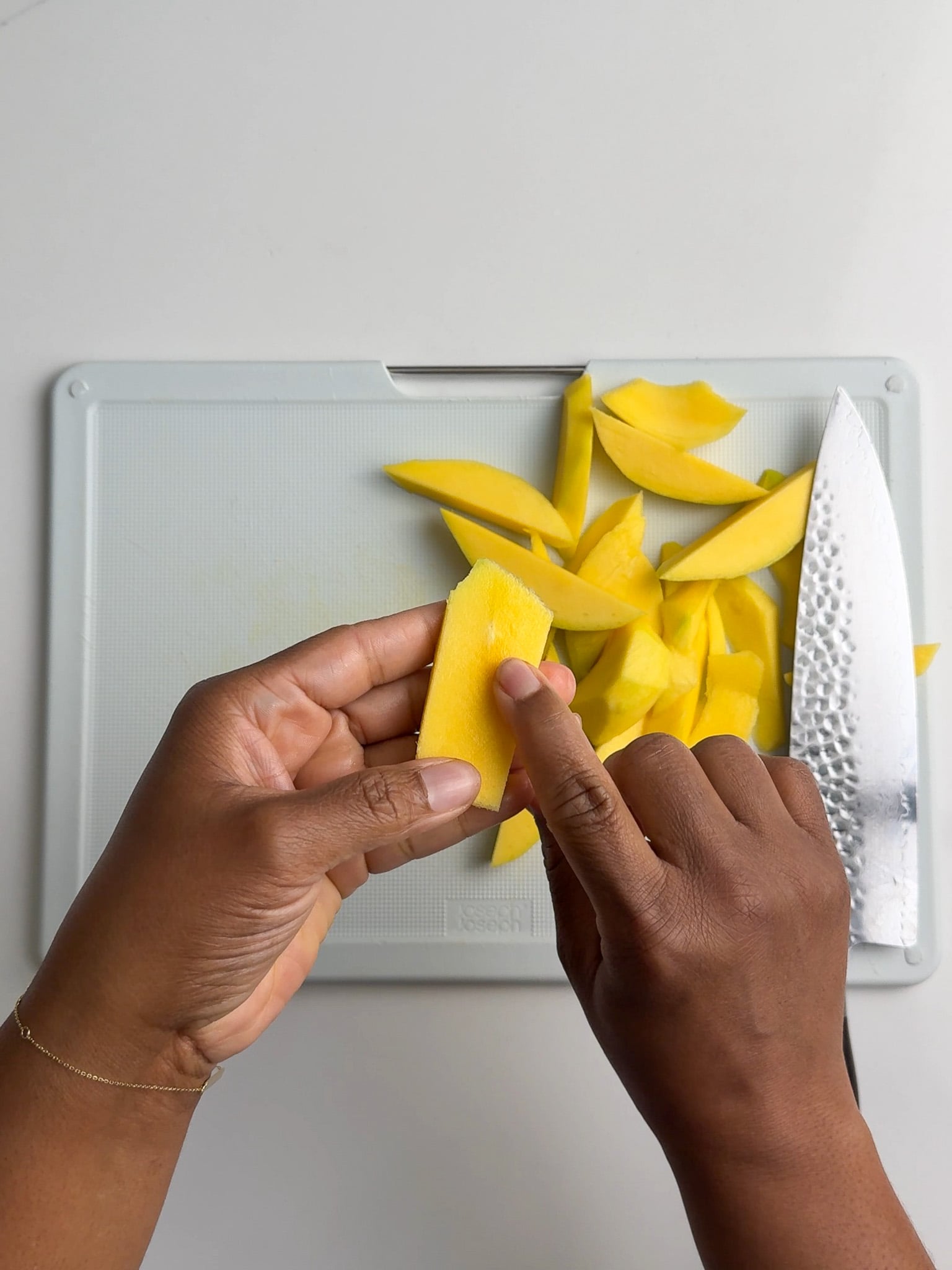 Hands slicing peeled green mango into thin strips on a white cutting board.