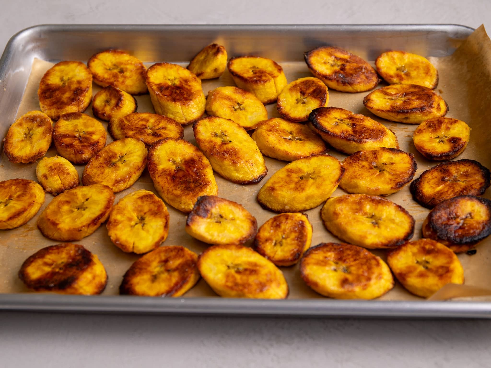 A close-up of oven baked plantain slices showing golden brown, slightly crisp edges on a sheet pan.