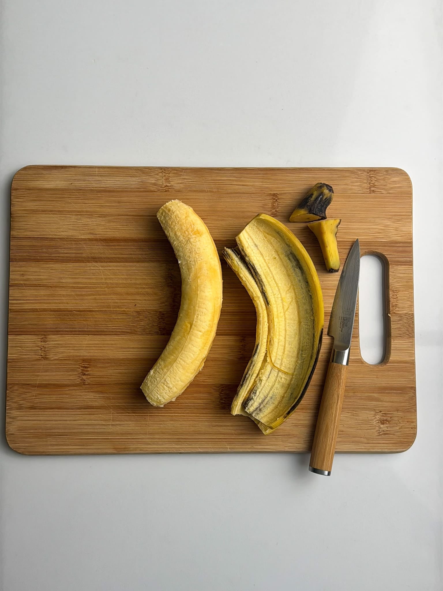 Whole ripe plantains sit on a cutting board next to a knife, ready to be prepped.