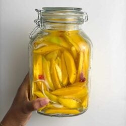 Hand holding a jar filled with pickled mango slices and brine.