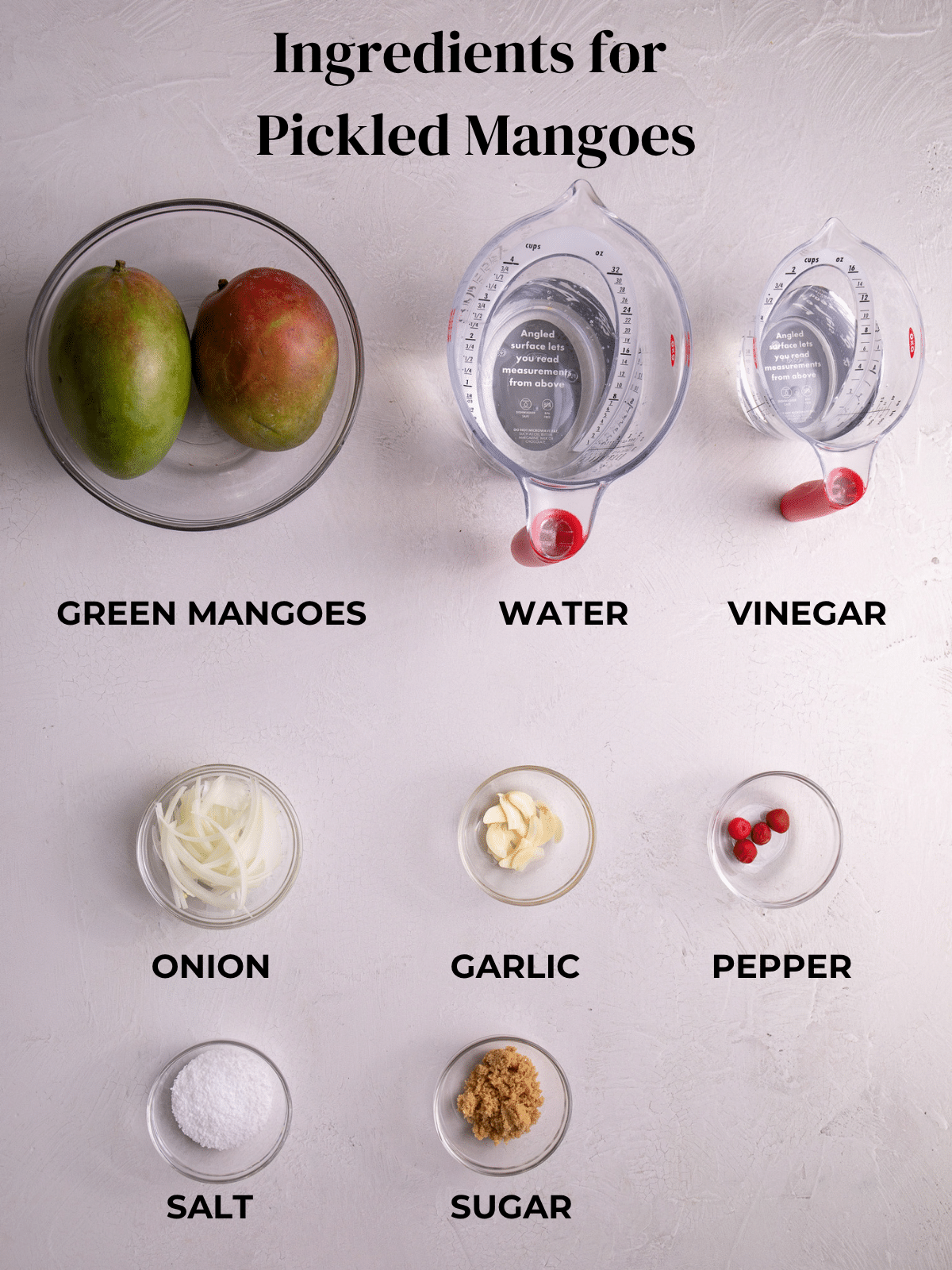 A flat-lay image titled “Ingredients for Pickled Mangoes” shows neatly arranged ingredients on a light surface. At the top left are two whole green mangoes in a glass bowl. To the right are measuring cups filled with water and vinegar. Below them are small bowls containing sliced onion, garlic cloves, and whole red peppers. At the bottom are bowls of salt and brown sugar. Each ingredient is labeled in bold text beneath it.