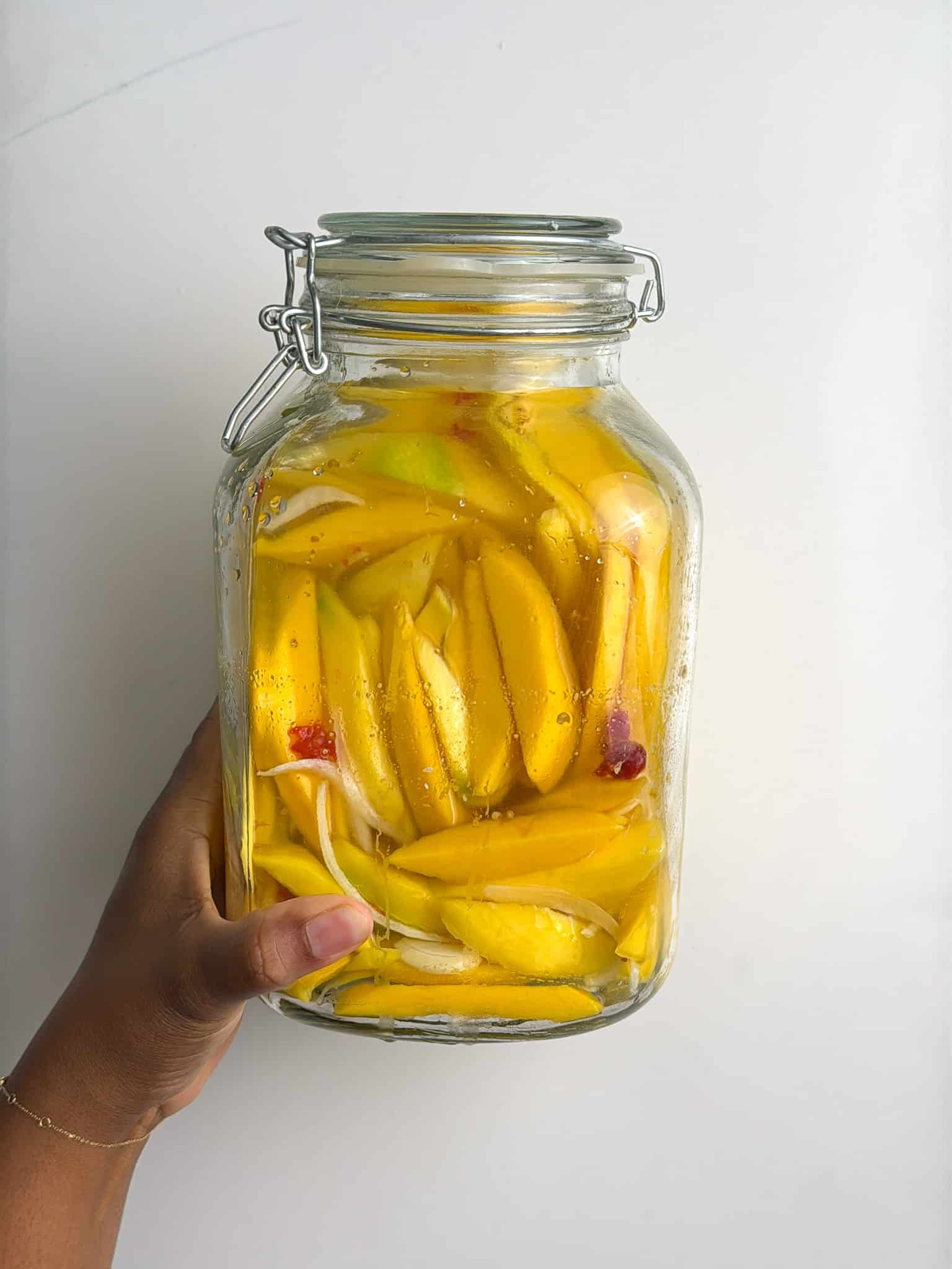 Hand holding a jar filled with pickled mango slices and brine.