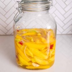 Jar of pickled mango with onions and peppers in brine on a countertop.