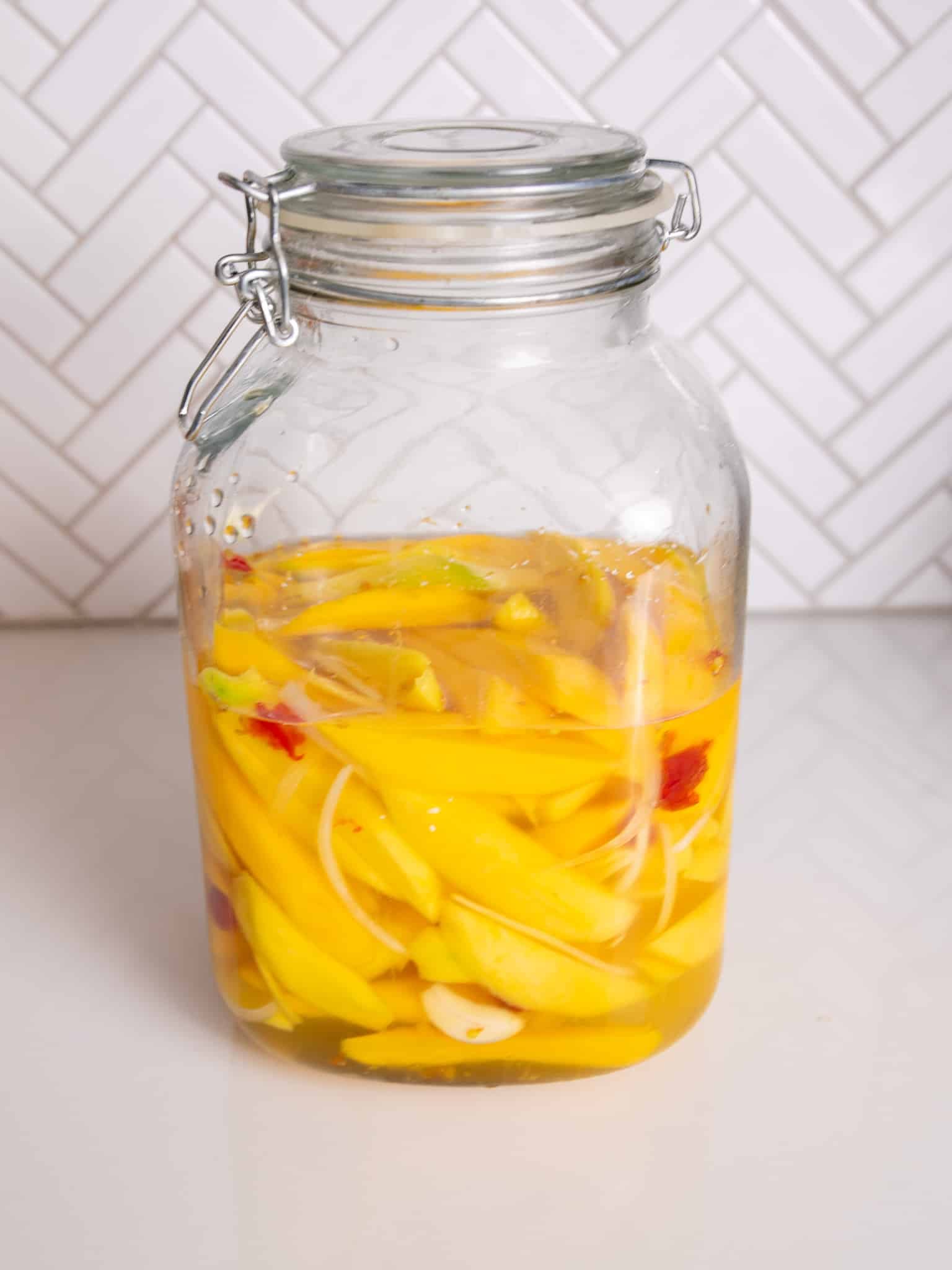 Jar of pickled mango with onions and peppers in brine on a countertop.