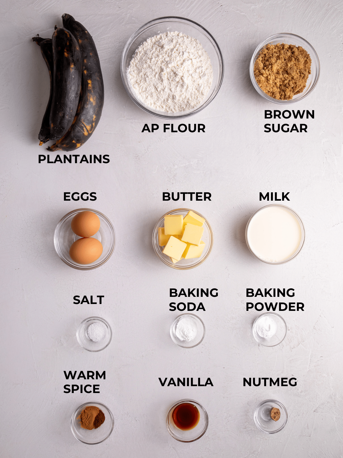 Ingredients for plantain bread laid out, including plantains, flour, eggs, butter, milk, and spices.