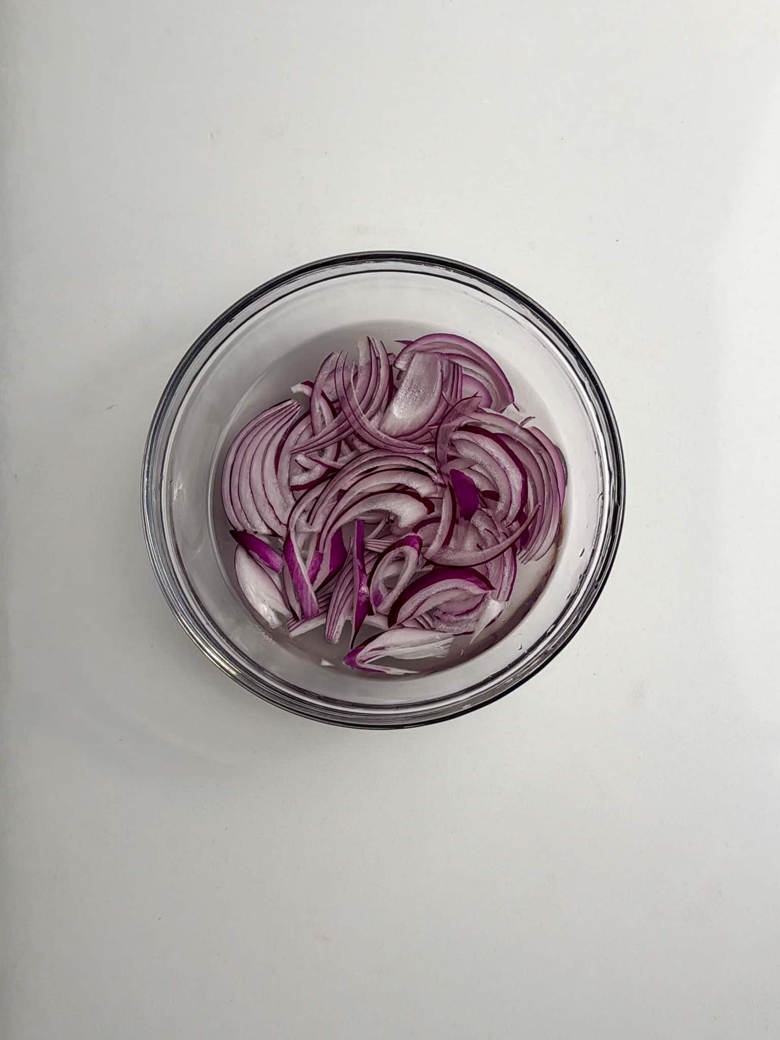A small glass bowl filled with thinly sliced red onions.