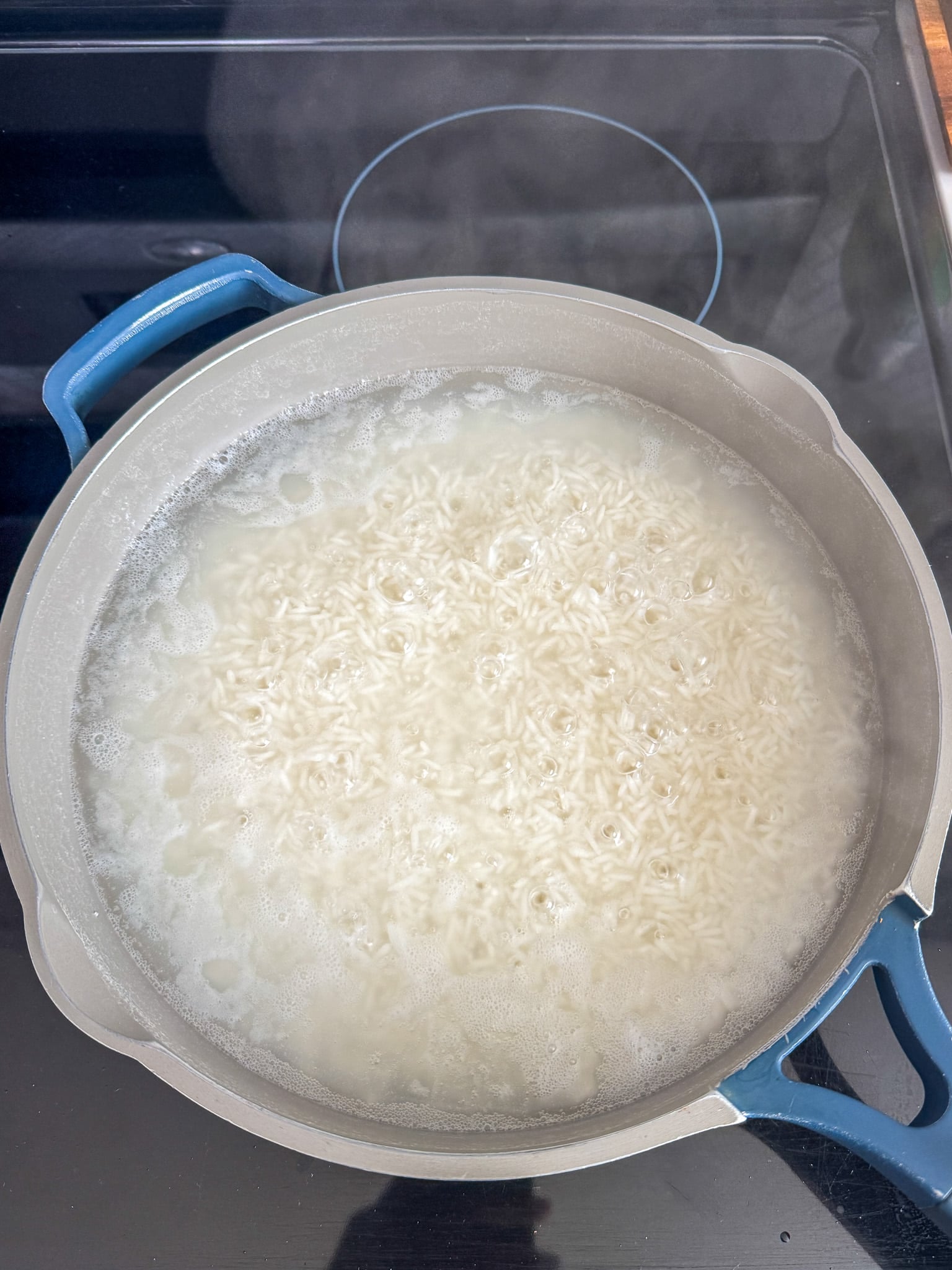 White rice boiling in water in a pot on the stovetop, with bubbles forming on the surface.