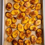 A full tray of roasted plantains arranged in a single layer with evenly browned surfaces.