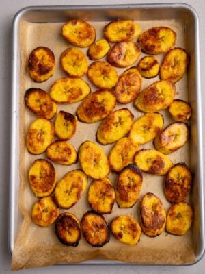 A full tray of roasted plantains arranged in a single layer with evenly browned surfaces.