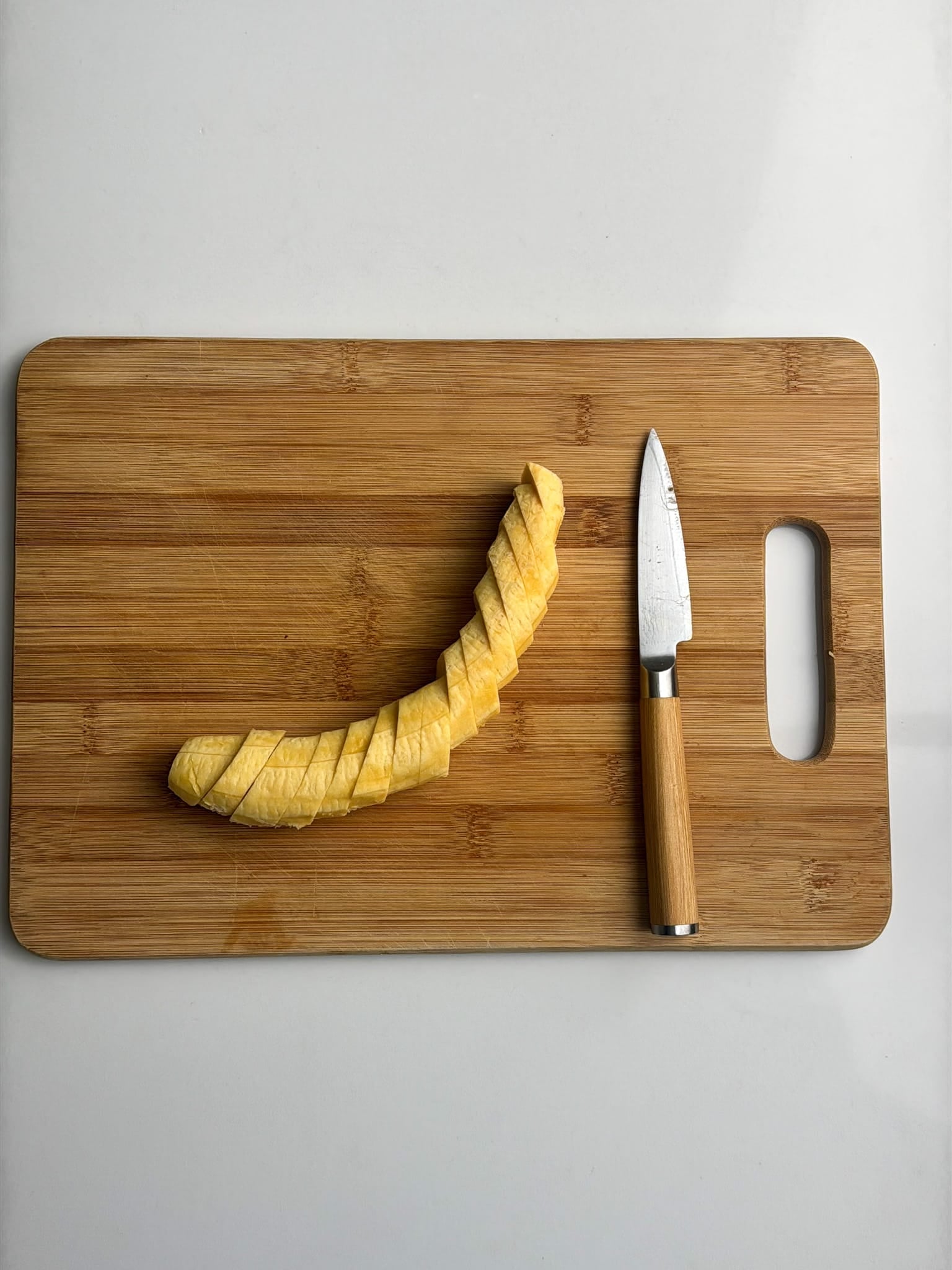 A peeled plantain is sliced on a cutting board next to a knife.