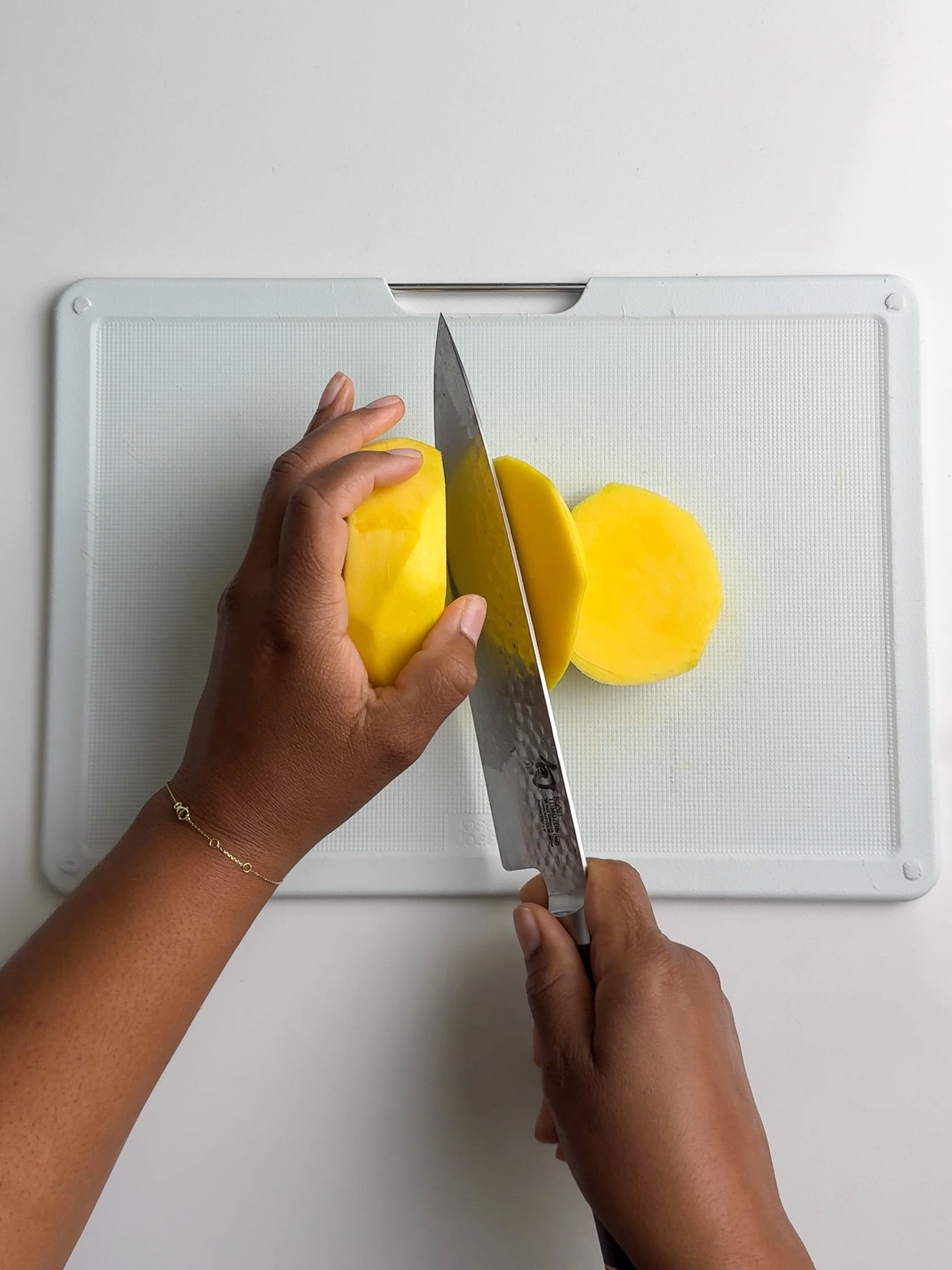 A knife cutting into a peeled green mango on a cutting board.